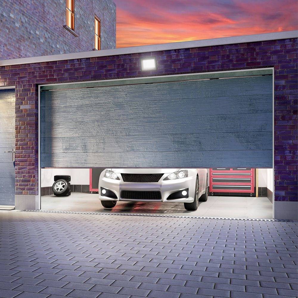 Ein Auto parkt in einer halb geöffneten Garage bei Sonnenuntergang. Eine rote Werkzeugbank ist im Hintergrund sichtbar.