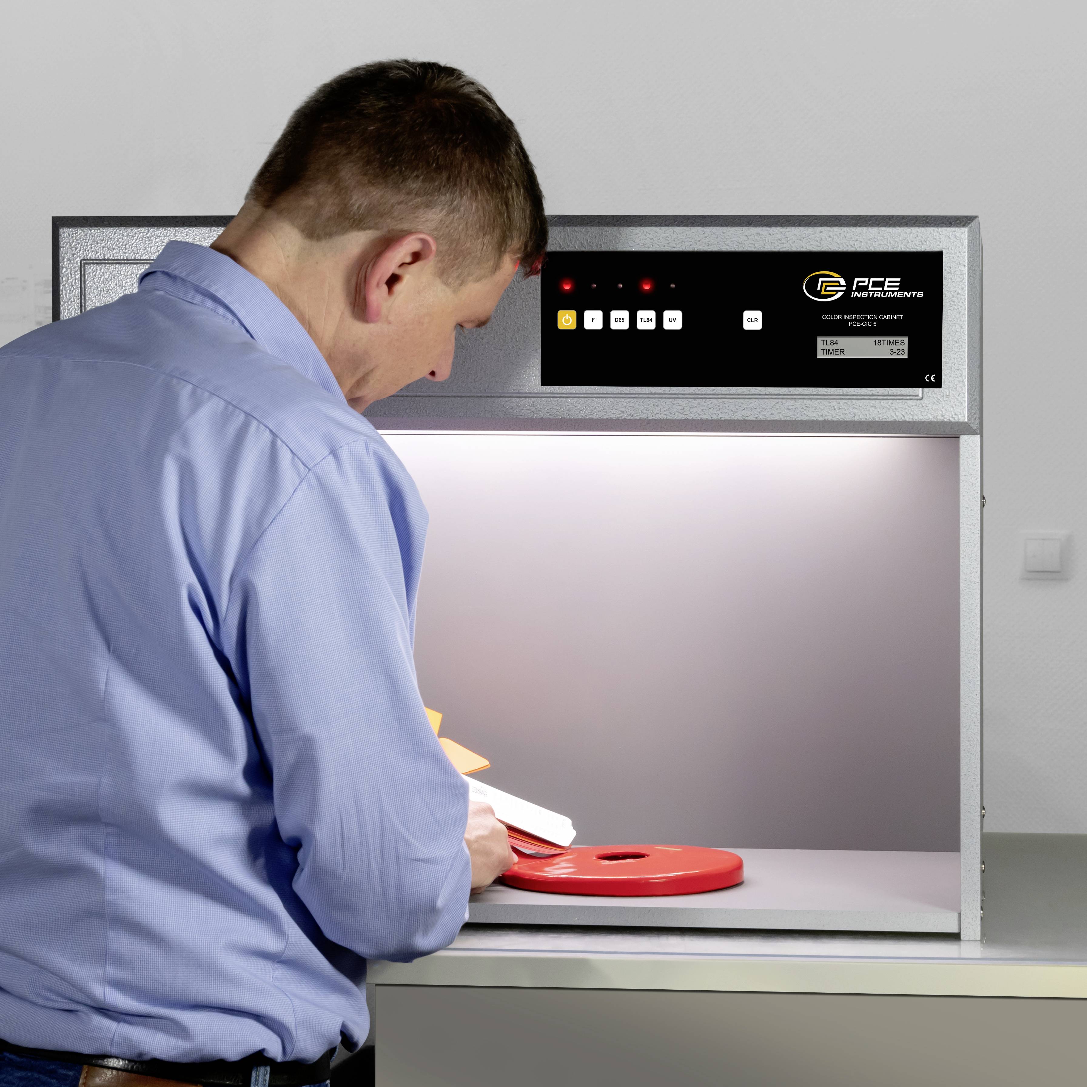 Ein Mann untersucht ein Objekt unter einem Lichtprüfgerät, das zur Prüfung der Farbkonsistenz dient.