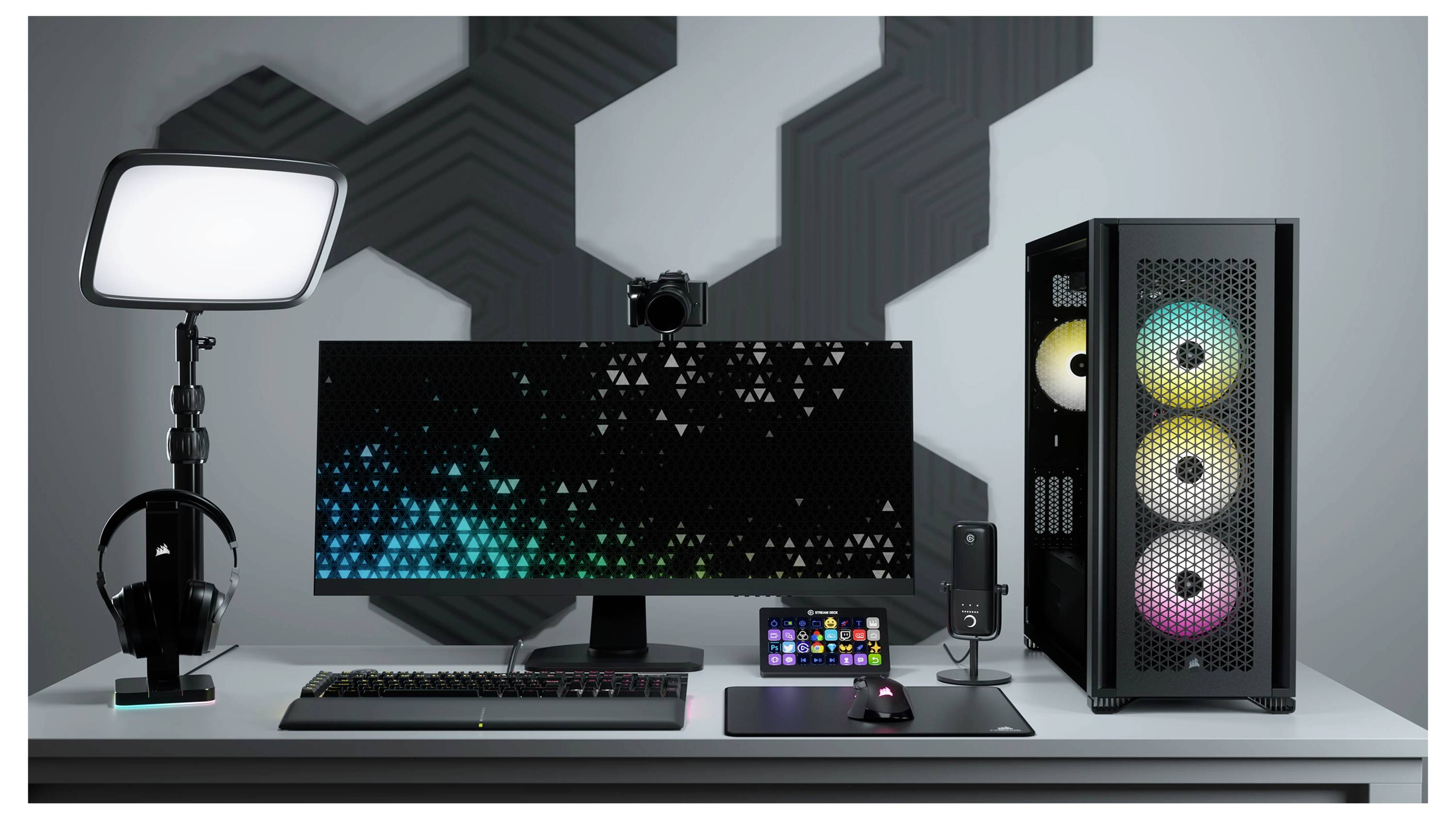 Setup für Streaming: Computer mit RGB-Beleuchtung, Monitor, Tastatur, Mikrofon, Kameralicht und Headset auf einem Schreibtisch.
