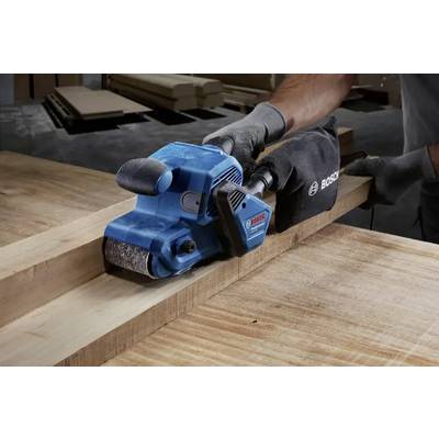 Eine Person verwendet einen blauen Bosch-Bandschleifer auf einem Holzbrett mit Präzision und veranschaulicht damit Holzbearbeitungswerkzeuge und Handwerkskunst in Aktion.