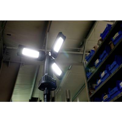 Ein heller, vierarmiger LED-Strahler leuchtet in einem Lagerraum mit blauen Regalen im Hintergrund.