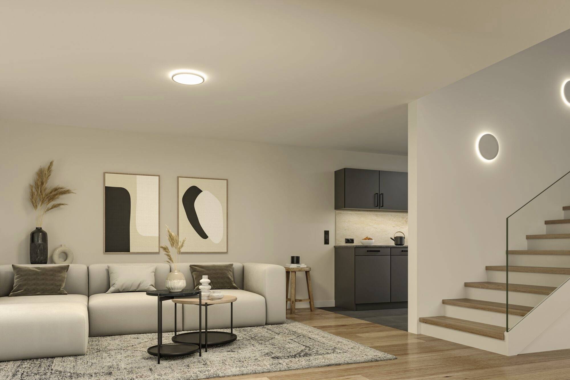 Modernes Wohnzimmer mit beiger Couch, zwei abstrakten Kunstwerken an der Wand, runden Couchtischen und offener Küche im Hintergrund.