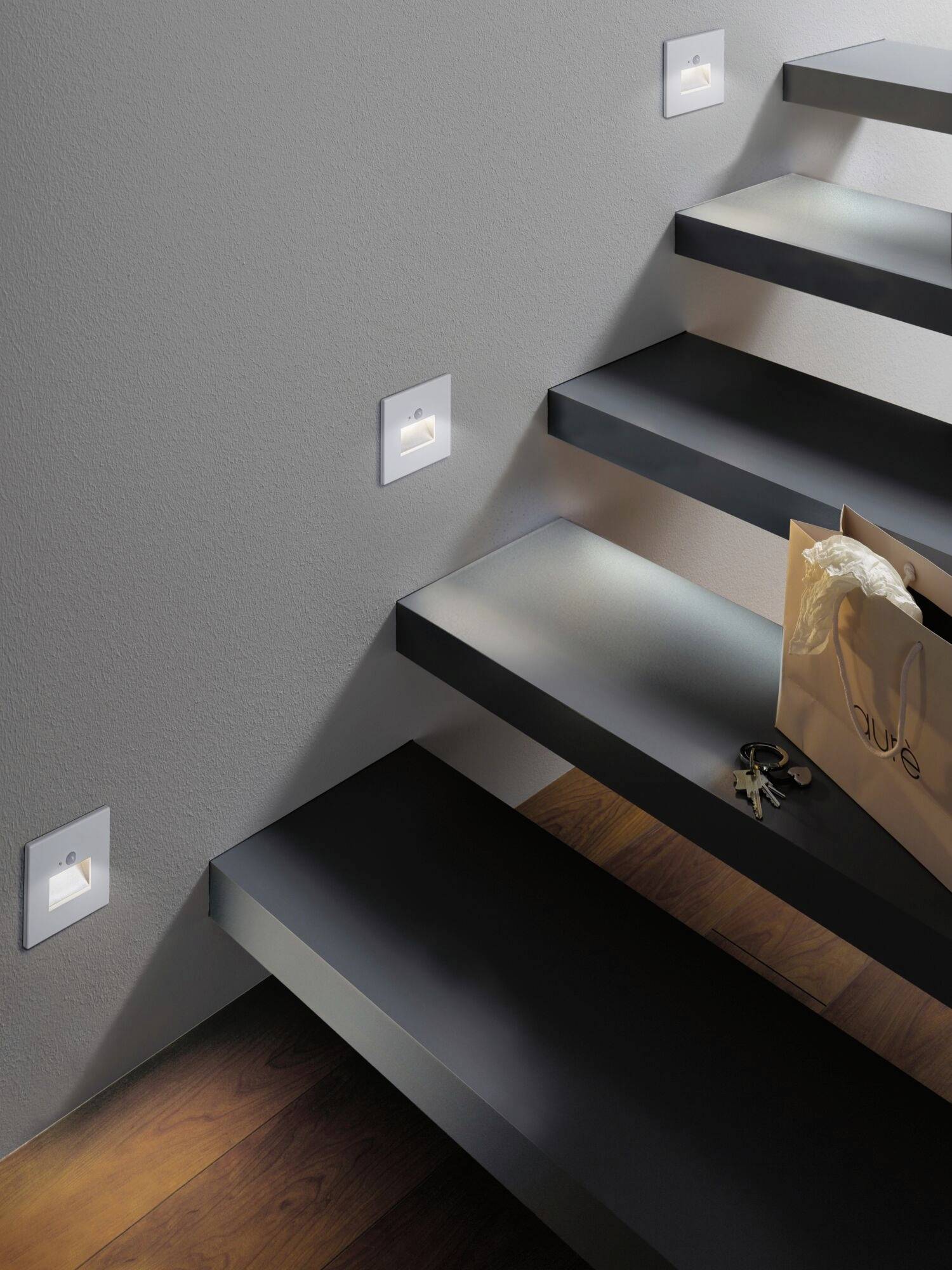Eine modern gestaltete Treppe mit stufenbeleuchteten LED-Leuchten an der Wand, eine Einkaufstasche und ein Schlüsselbund auf der untersten Stufe.