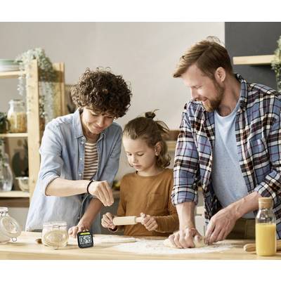Eine Familie backt zusammen in der Küche. Ein Erwachsener streut Mehl, ein Kind rollt den Teig aus, und ein weiterer Erwachsener hilft dabei.