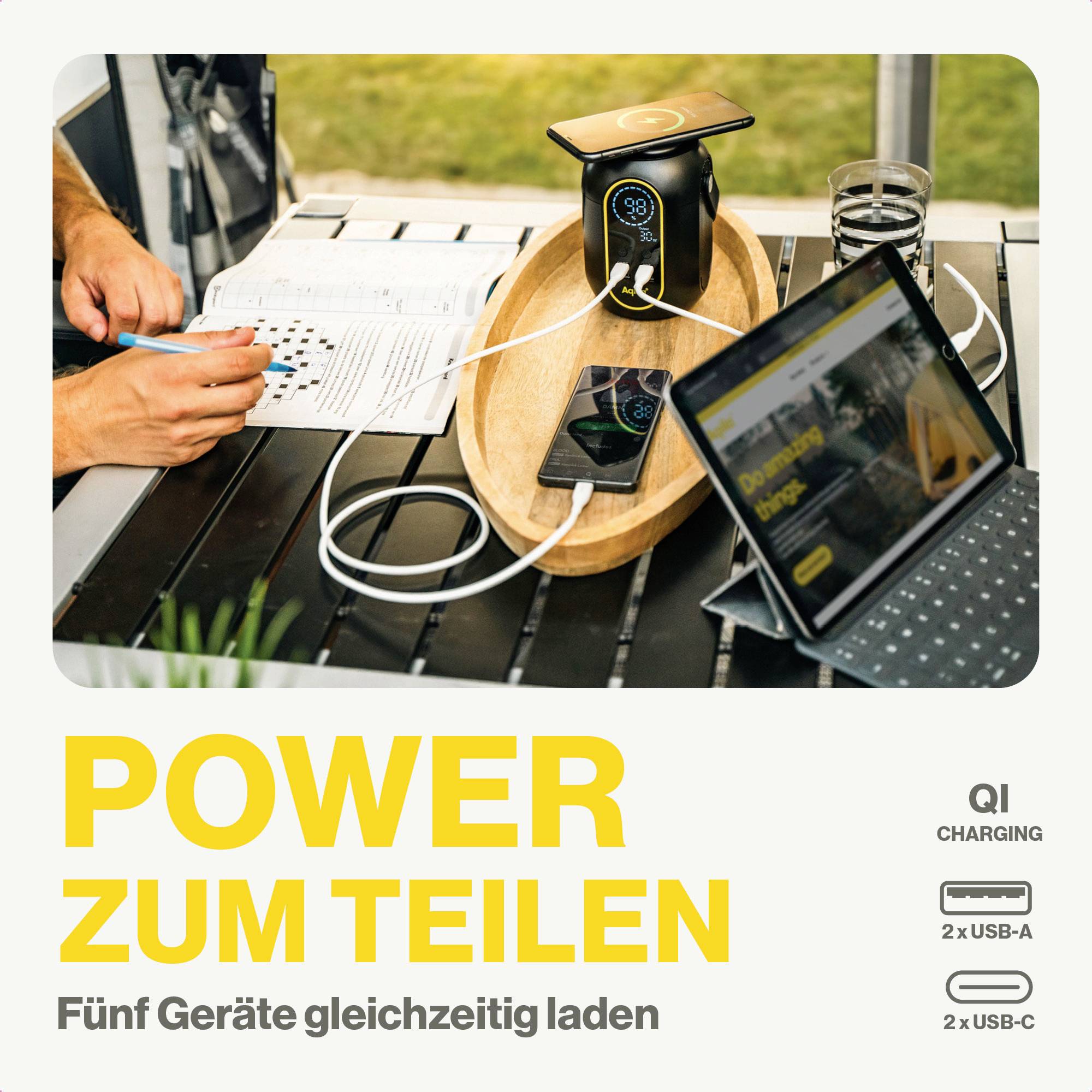'Power zum Teilen' zeigt ein Ladegerät mit mehreren Anschlüssen, das fünf Geräte gleichzeitig laden kann. Im Hintergrund ein Tablet und ein Smartphone.