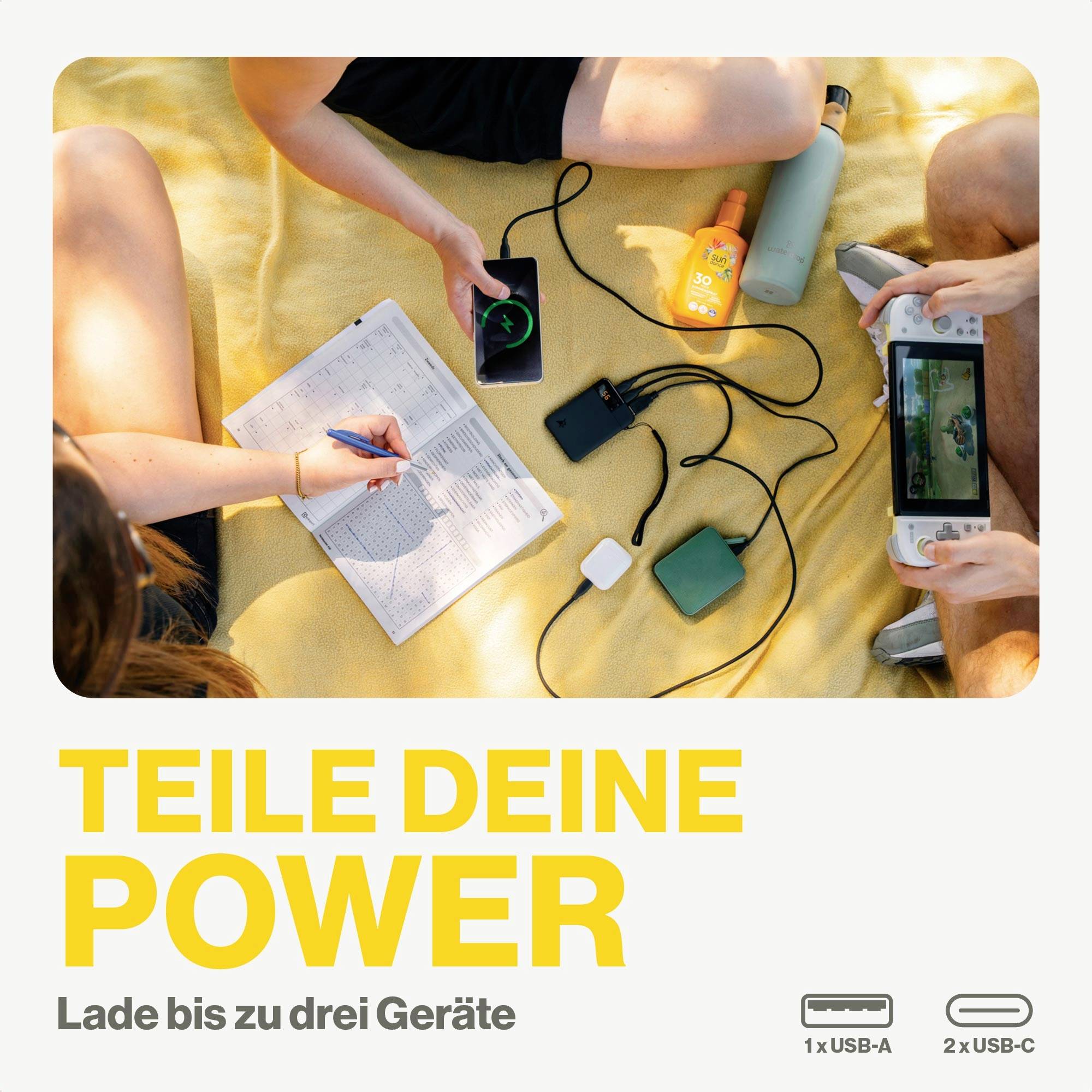 Personen sitzen auf einer Decke, teilen tragbare Ladegeräte. Text 'TEILE DEINE POWER', lädt bis zu drei Geräte.