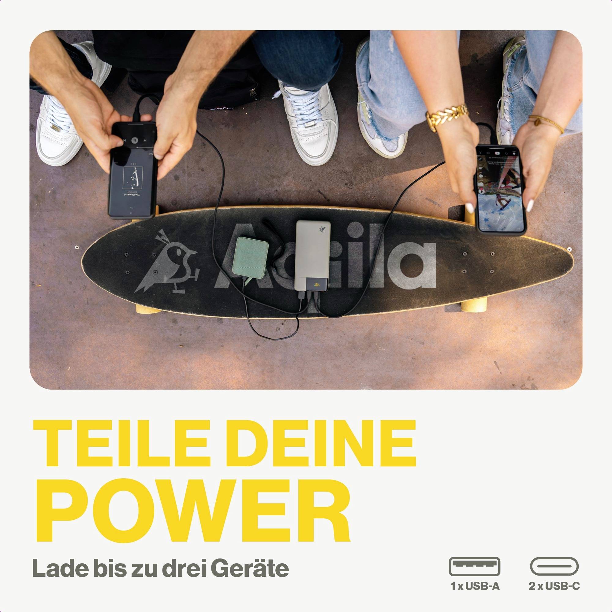 Zwei Personen laden drei Geräte auf einem Skateboard mit Powerbank. Text: 'Teile deine Power. Lade bis zu drei Geräte.'