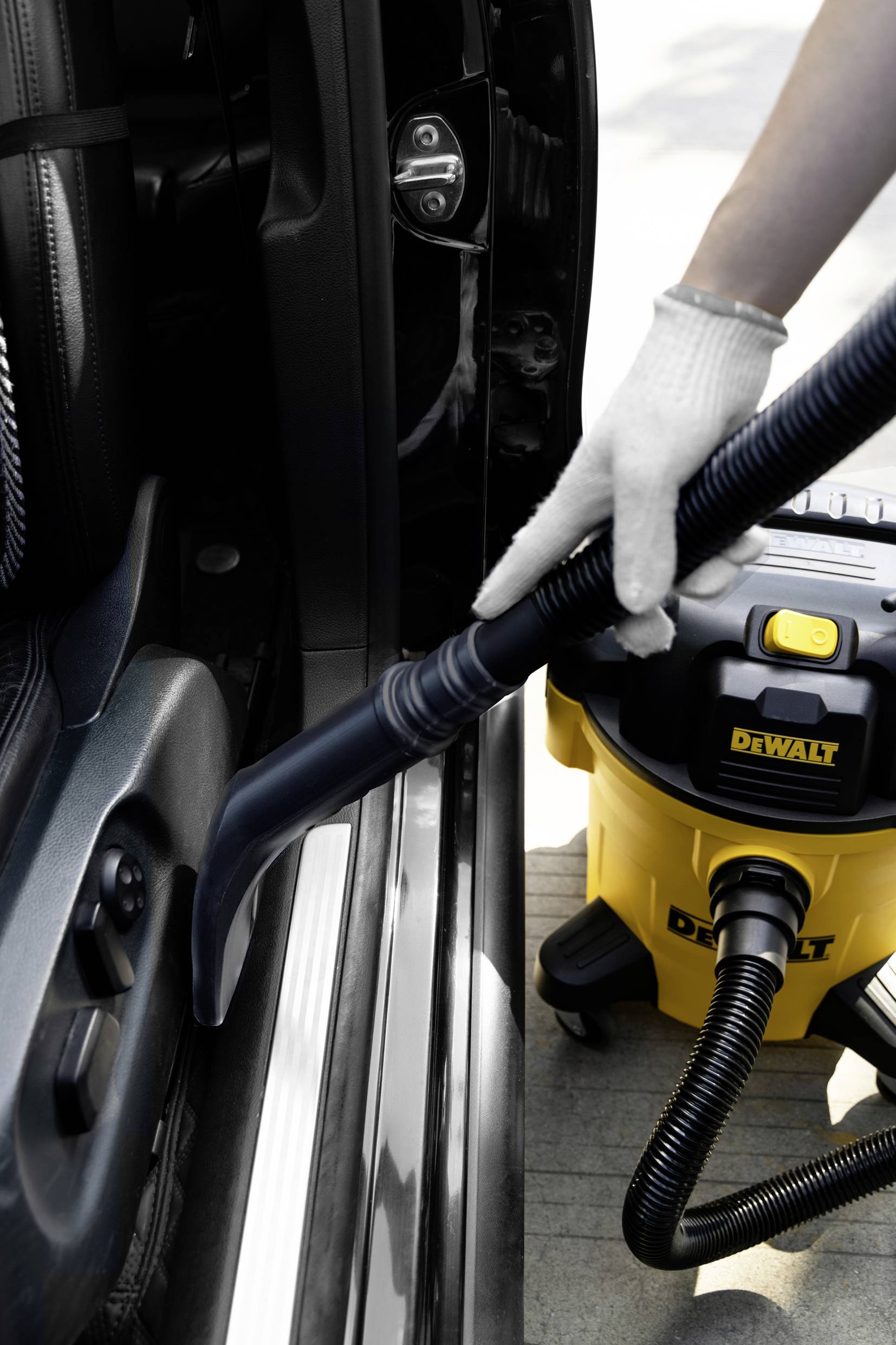 Eine Person saugt mit einem gelben Staubsauger den Innenraum eines Autos. Der Fokus liegt auf dem Reinigen des Türbereichs.
