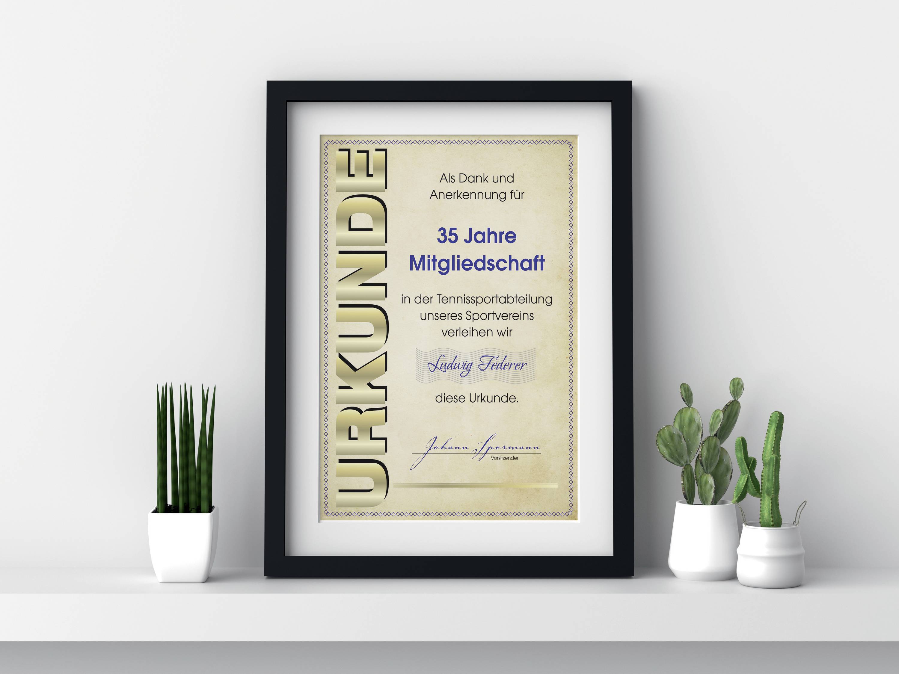 Ein gerahmter Tennis-Verdienstpreis mit der Aufschrift '35 Jahre Mitgliedschaft'. Daneben drei kleine Pflanztöpfe auf einem weißen Tisch.