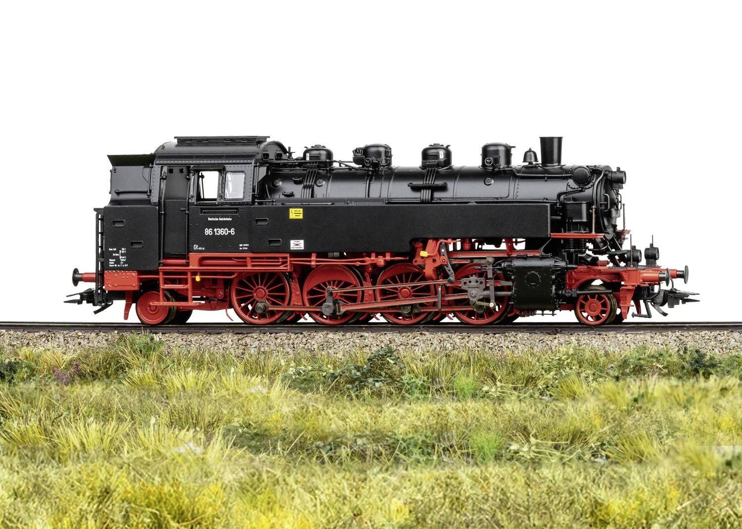 Dampflokomotive auf einem Gleis, seitliches Profil. Schwarzer Kesselaufbau mit rotem Fahrwerk. Umgeben von Gras.