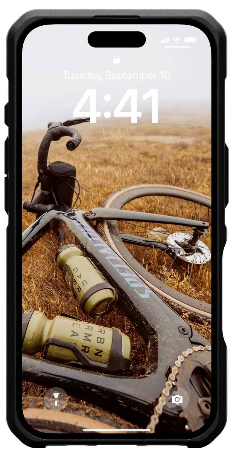 Ein Smartphone zeigt einen Startbildschirm mit Datum und Uhrzeit. Im Hintergrund liegt ein Fahrrad auf einem Feld.