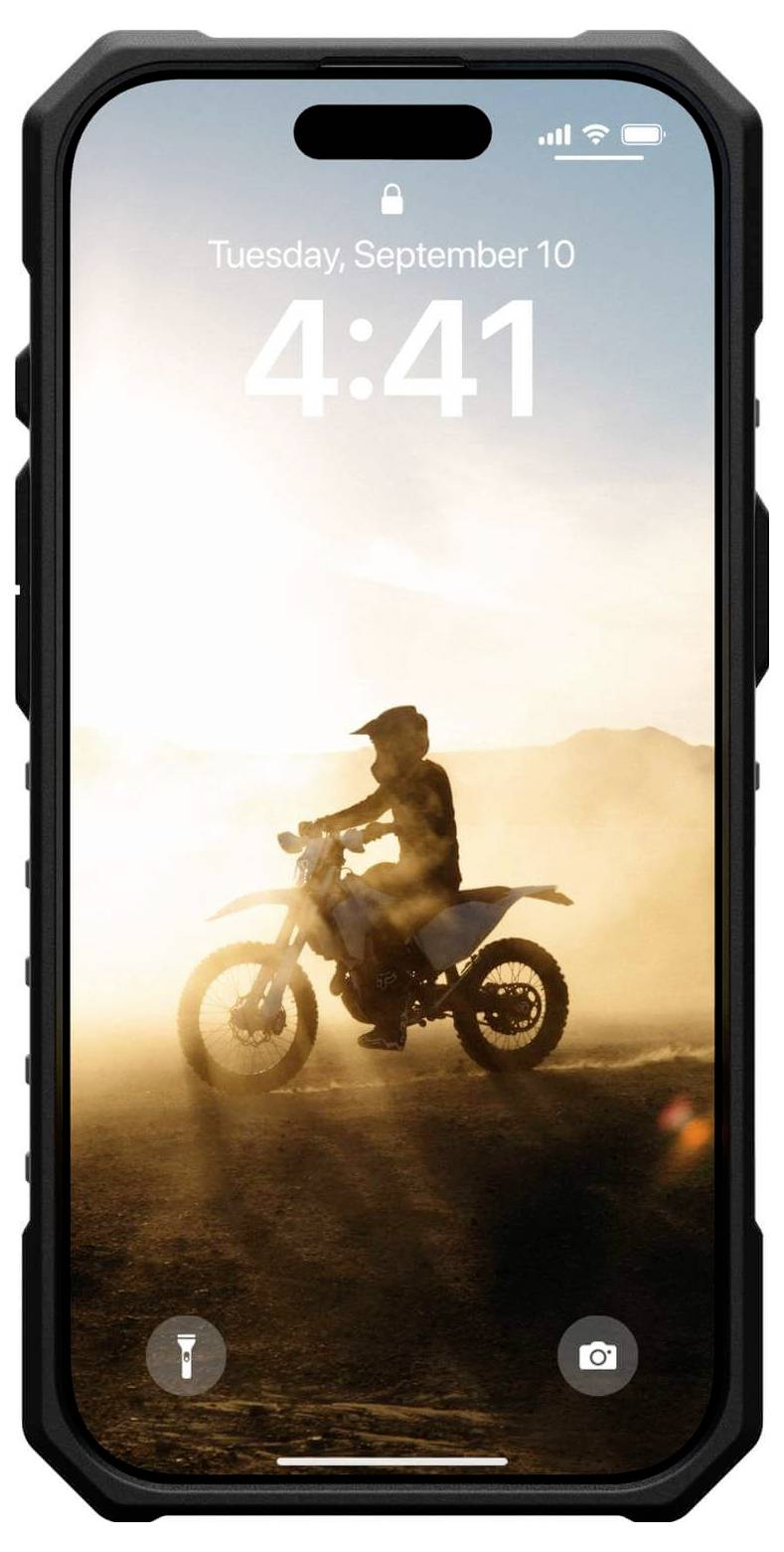 Eine Person fährt auf einem Motorrad durch eine staubige Wüstenlandschaft. Der Himmel ist klar, und die Uhrzeit auf dem Handy-Display zeigt 4:41.