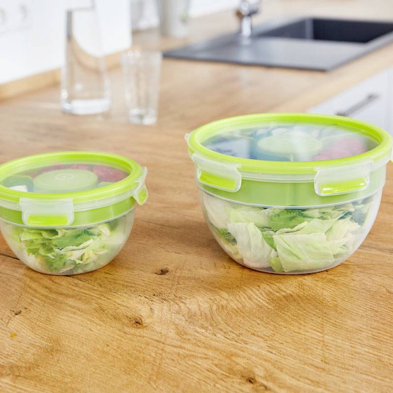 Zwei grüne Frischhalteboxen mit Salat auf einer Küchenarbeitsplatte, im Hintergrund eine Spüle. Links eine kleinere, rechts eine größere Box.