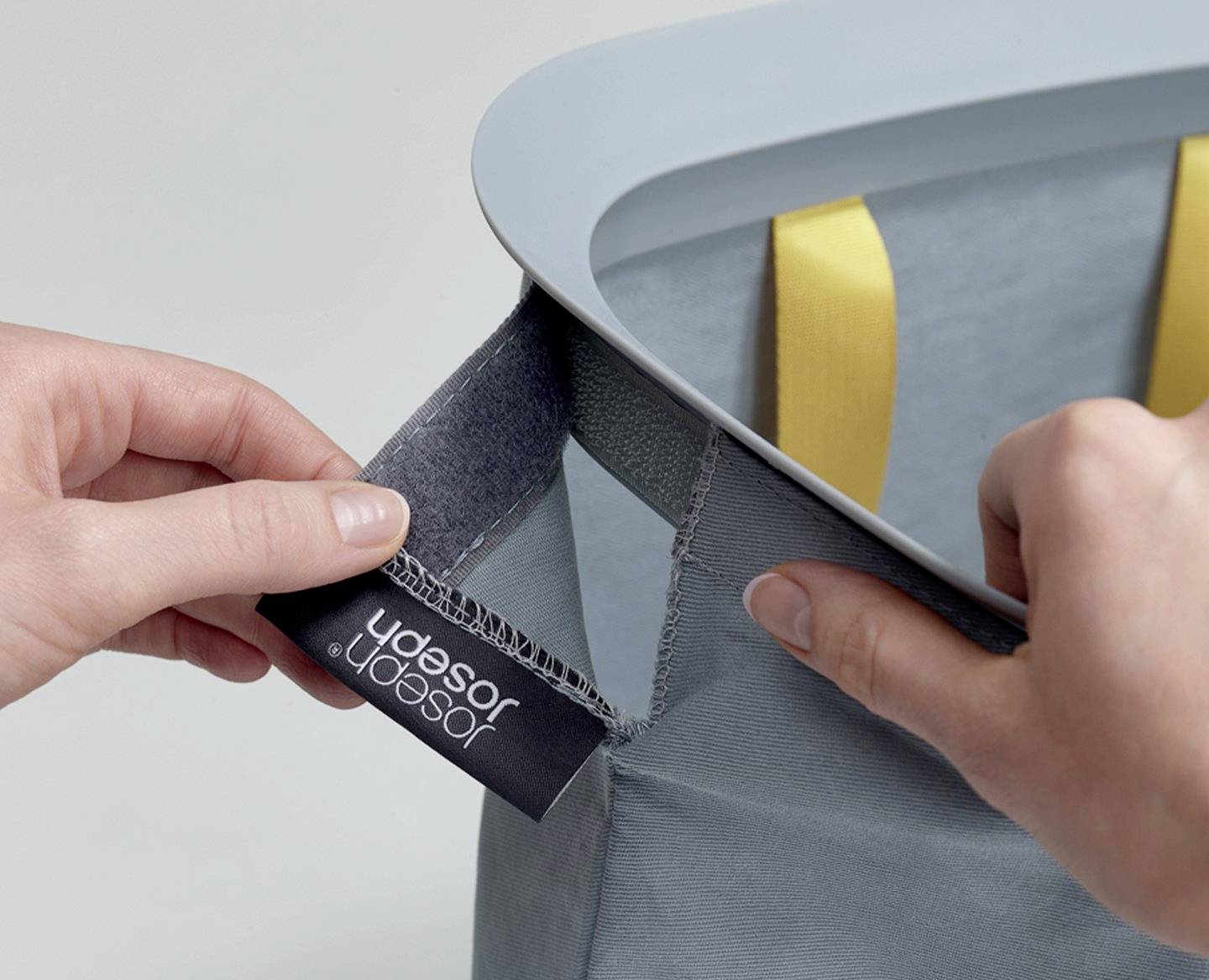 Eine Person befestigt ein Etikett mit der Aufschrift 'Jacob Jensen Design' an einer grauen Tasche mit gelben Griffen.
