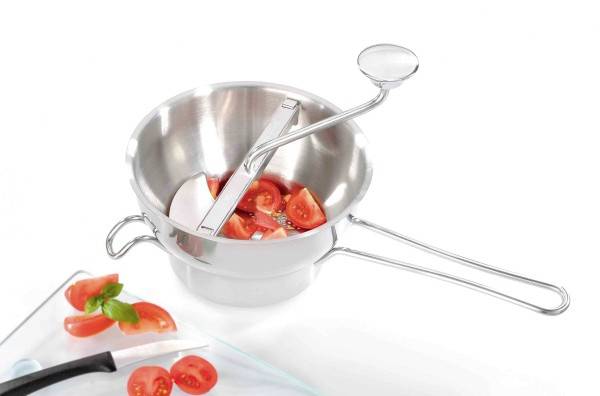 Metallene Passiermühle mit geschnittenen Tomaten und Zwiebeln innen; nebenbei ein Glasbrett mit Tomatenscheiben und Basilikum.