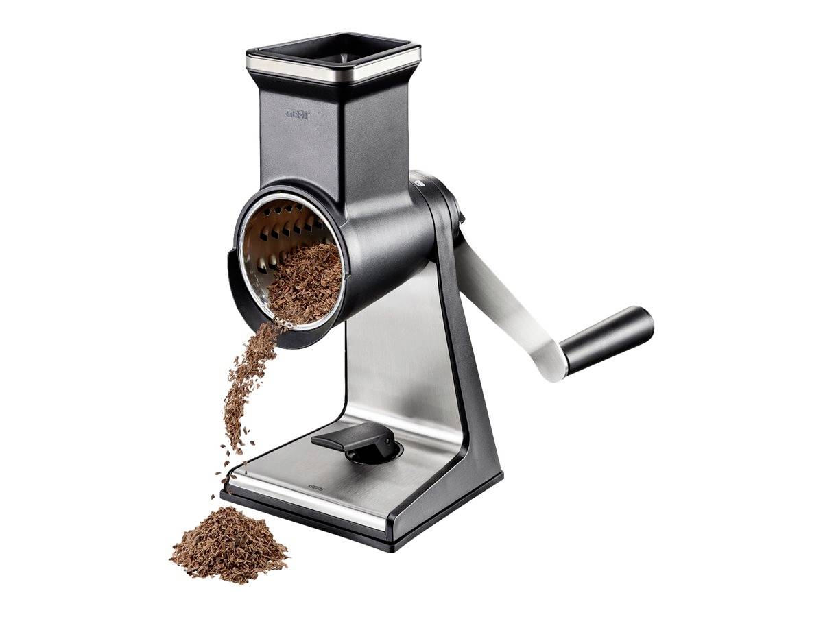 Manuelle Trommelreibe aus Metall mit Kurbel, aufrecht stehend. Schokolade wird durch die Reibe zerkleinert und fällt in einem Haufen heraus.