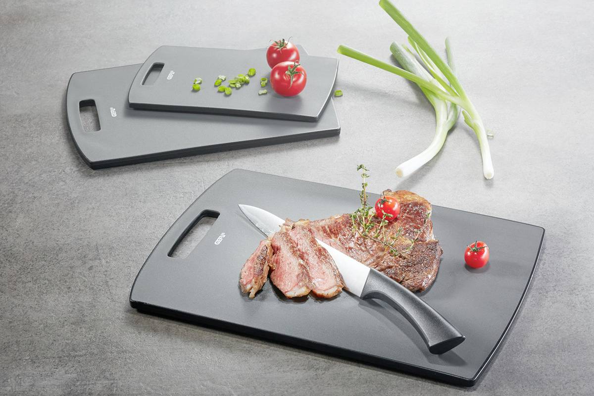 Drei Schneidebretter mit Speiseresten und einem Messer, dekoriert mit Tomaten und Frühlingszwiebeln. Hauptaugenmerk auf das mittlere Brett mit Fleisch.