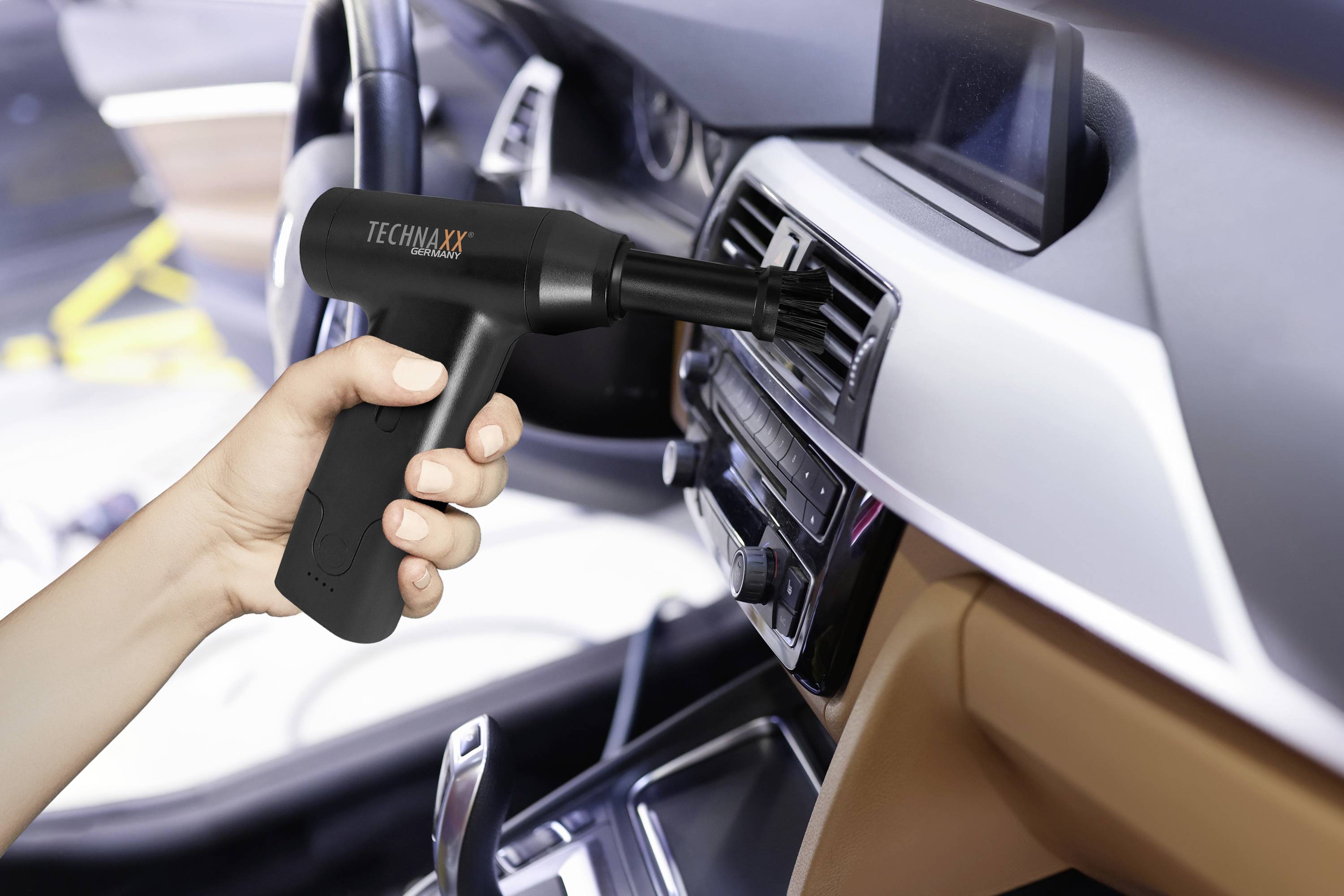 Eine Hand hält einen kleinen Staubsauger, der für die Reinigung eines Lüftungsschlitzes im Auto verwendet wird.