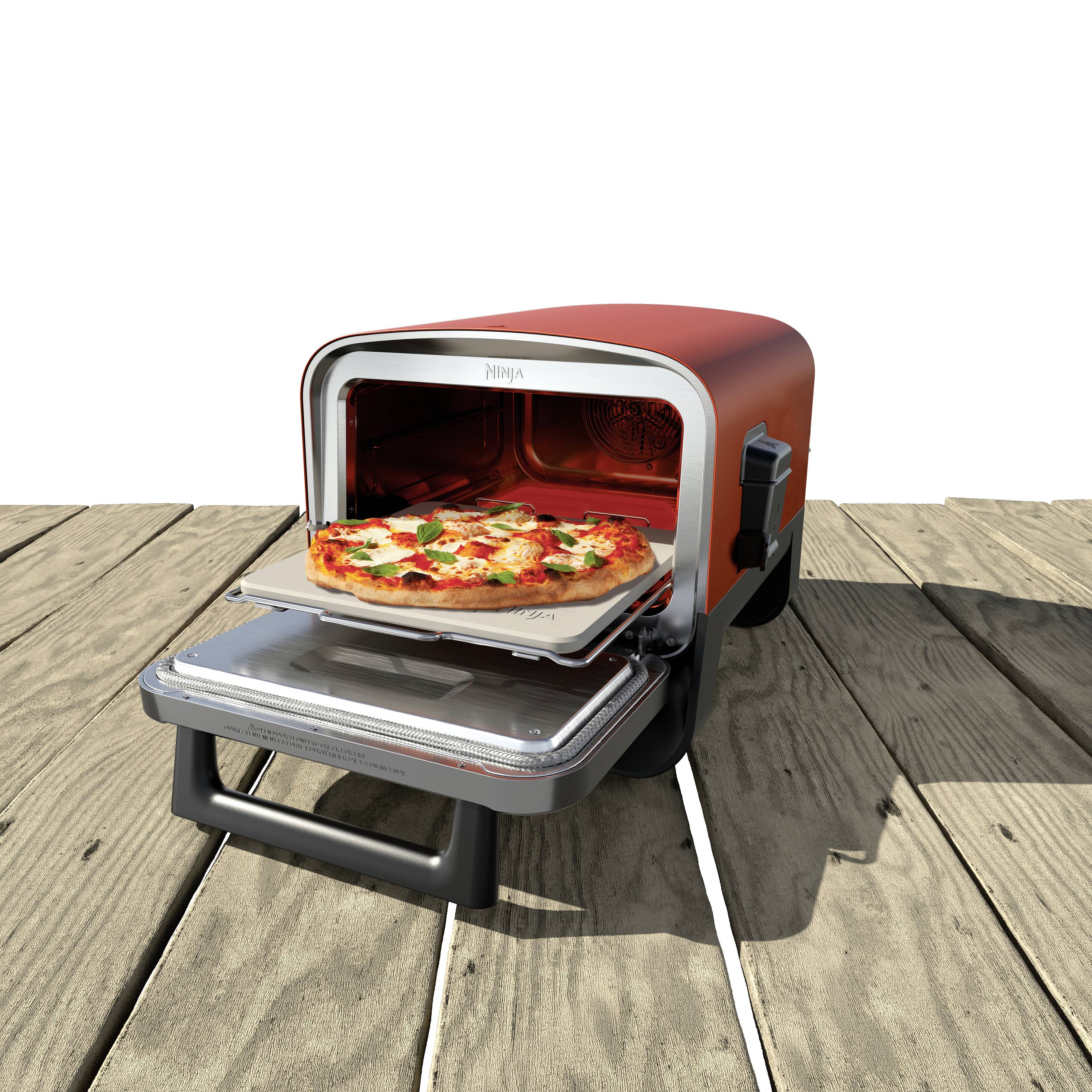 Ein roter, kleiner Ofen auf einer Holzoberfläche, backt gerade eine Pizza mit Käse und Gemüse. Die Ofentür ist offen, Pizza halb herausgezogen.
