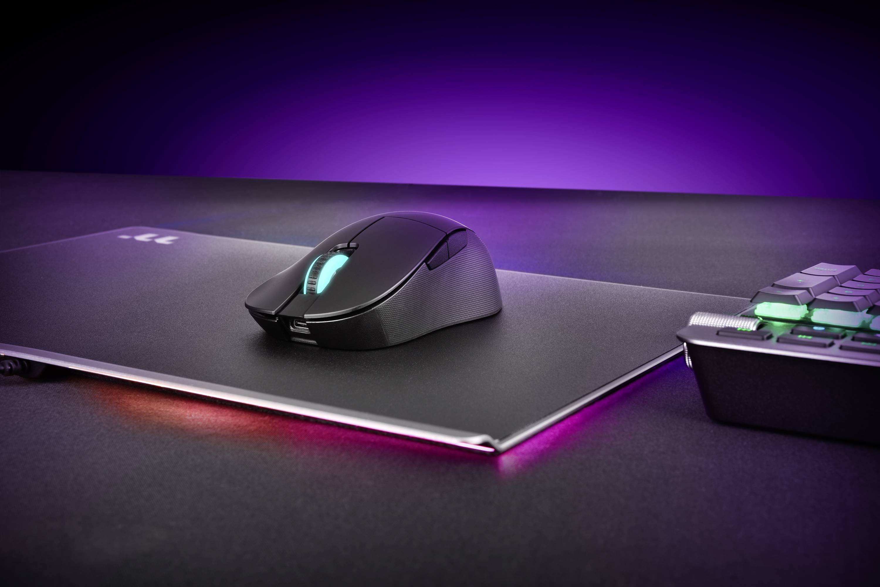 Eine kabellose Gaming-Maus liegt auf einem beleuchteten Mauspad neben einer teilweise sichtbaren Tastatur. Hintergrund ist violett.