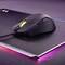 Eine schwarze Gaming-Maus mit einem leuchtend grünen Scrollrad liegt auf einem schwarzen Mauspad mit einem dezenten Pink- und Violett-Farbverlauf am Rand.