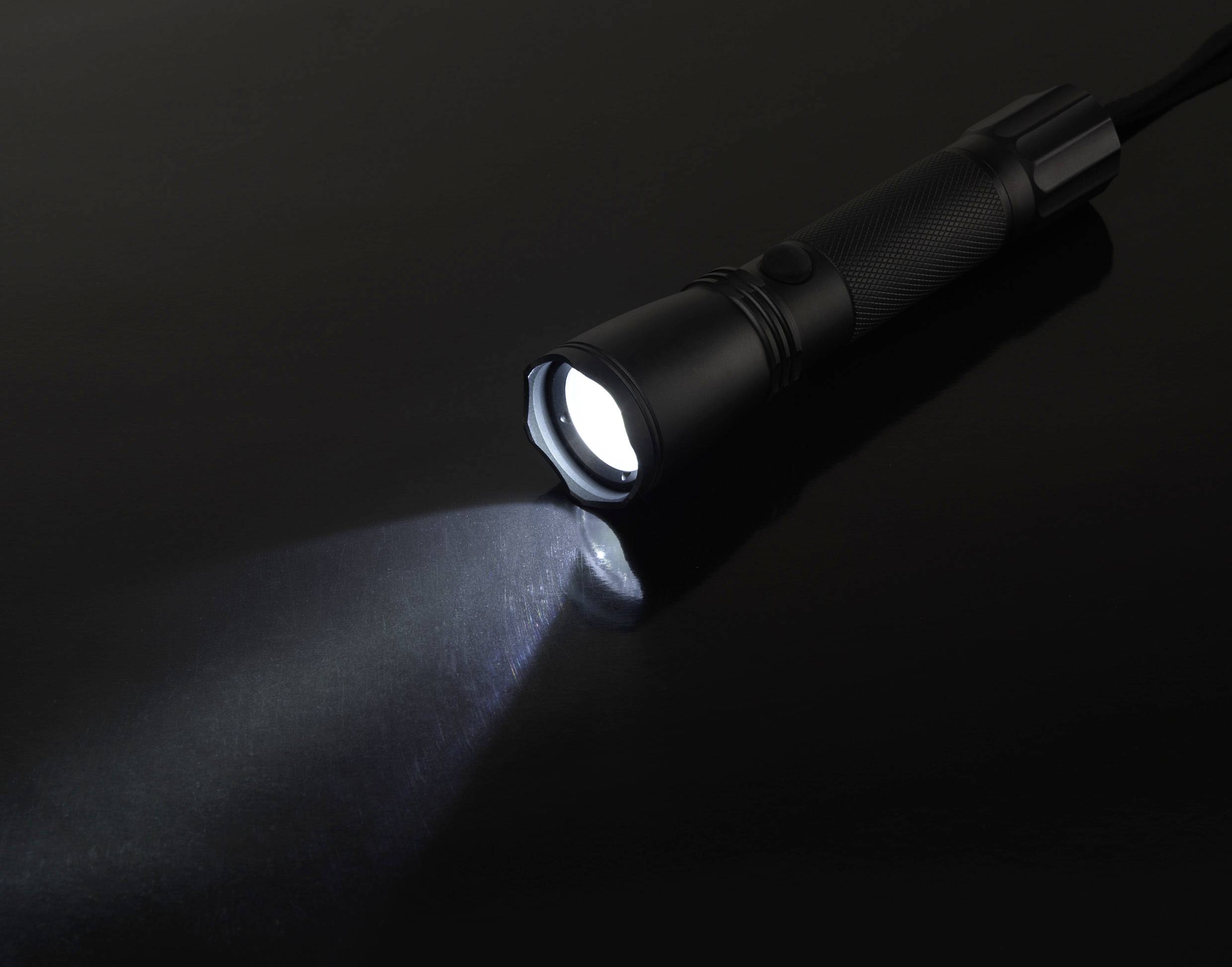 Eine Taschenlampe leuchtet auf einer dunklen Oberfläche. Das Licht erzeugt einen klaren, fokussierten Strahl nach vorne.