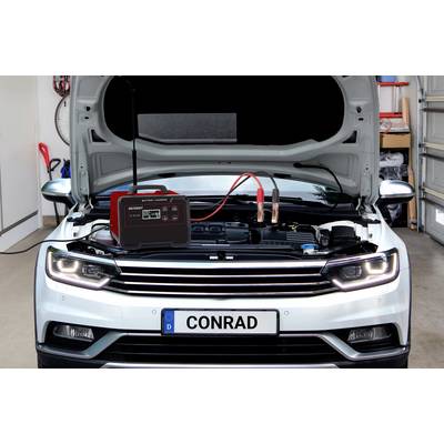 Ein weißes Auto mit geöffneter Motorhaube in einer Garage. Ein Ladegerät ist mit der Batterie verbunden.