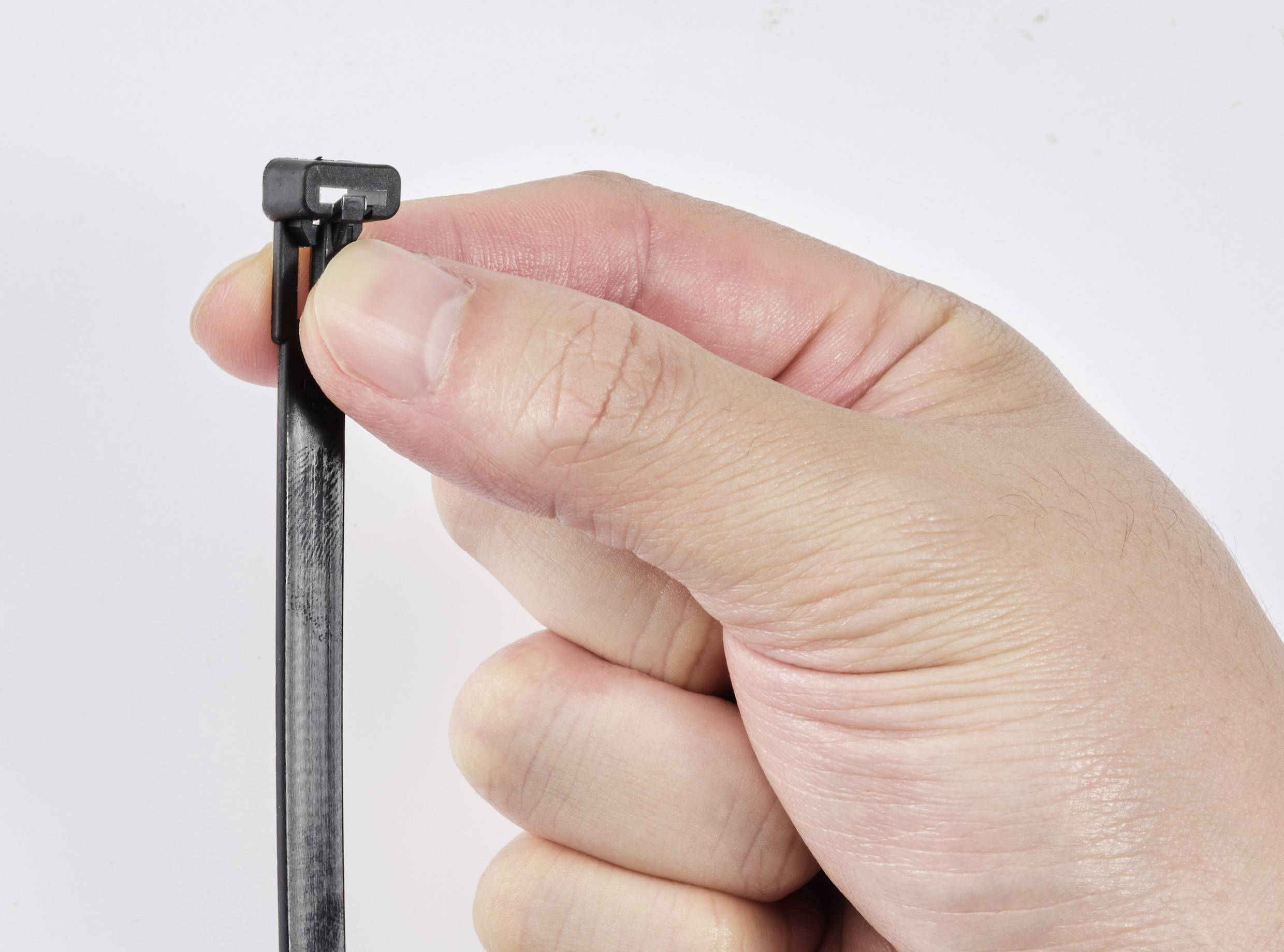 Eine Hand hält einen schwarzen Kabelbinder, der bereit ist, zusammengezogen zu werden. Detailaufnahme des Fingers auf dem Verschluss.