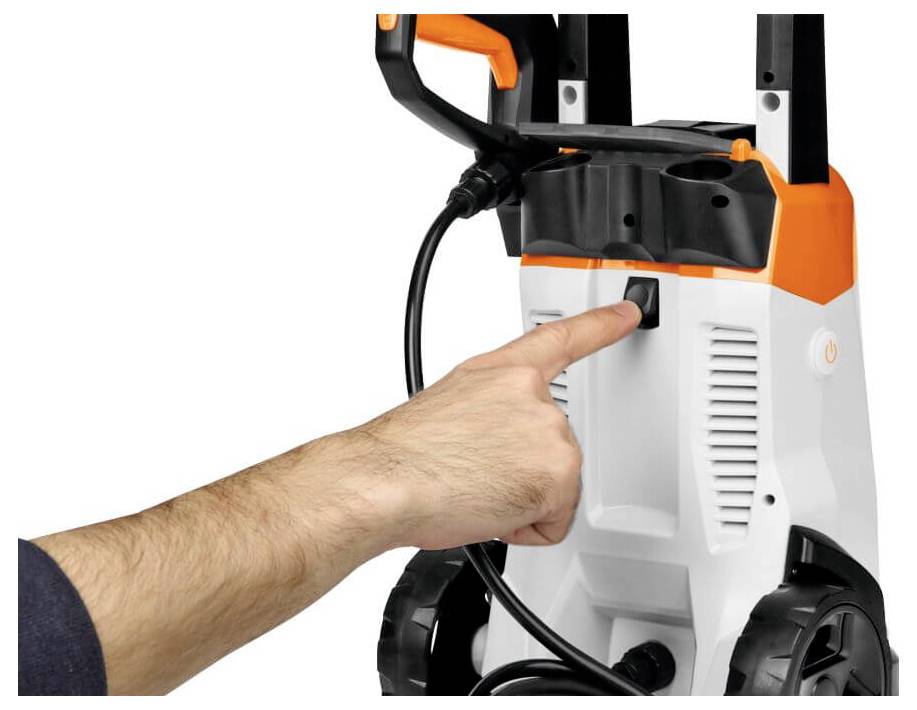 Eine Hand drückt den Einschaltknopf an einem Hochdruckreiniger. Gerät hat weiße und orangefarbene Details, mit einem schwarzen Griff und Kabel.