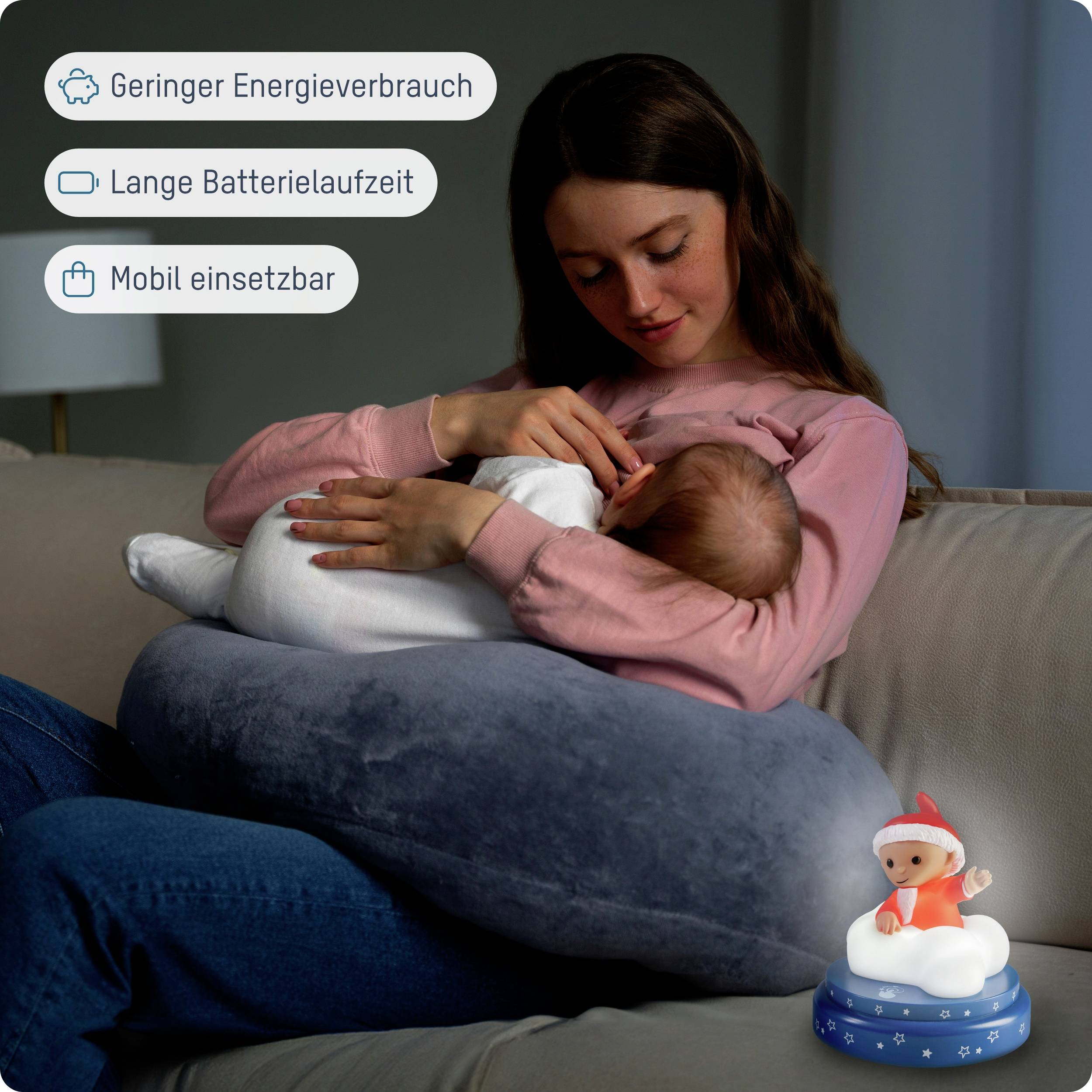 Eine Frau sitzt auf einem Sofa und hält ein Baby im Arm. Vor ihr steht ein Nachtlicht mit einem lächelnden Charakter darauf. Text: 'Geringer Energieverbrauch', 'Lange Batterielaufzeit', 'Mobil einsetzbar'.