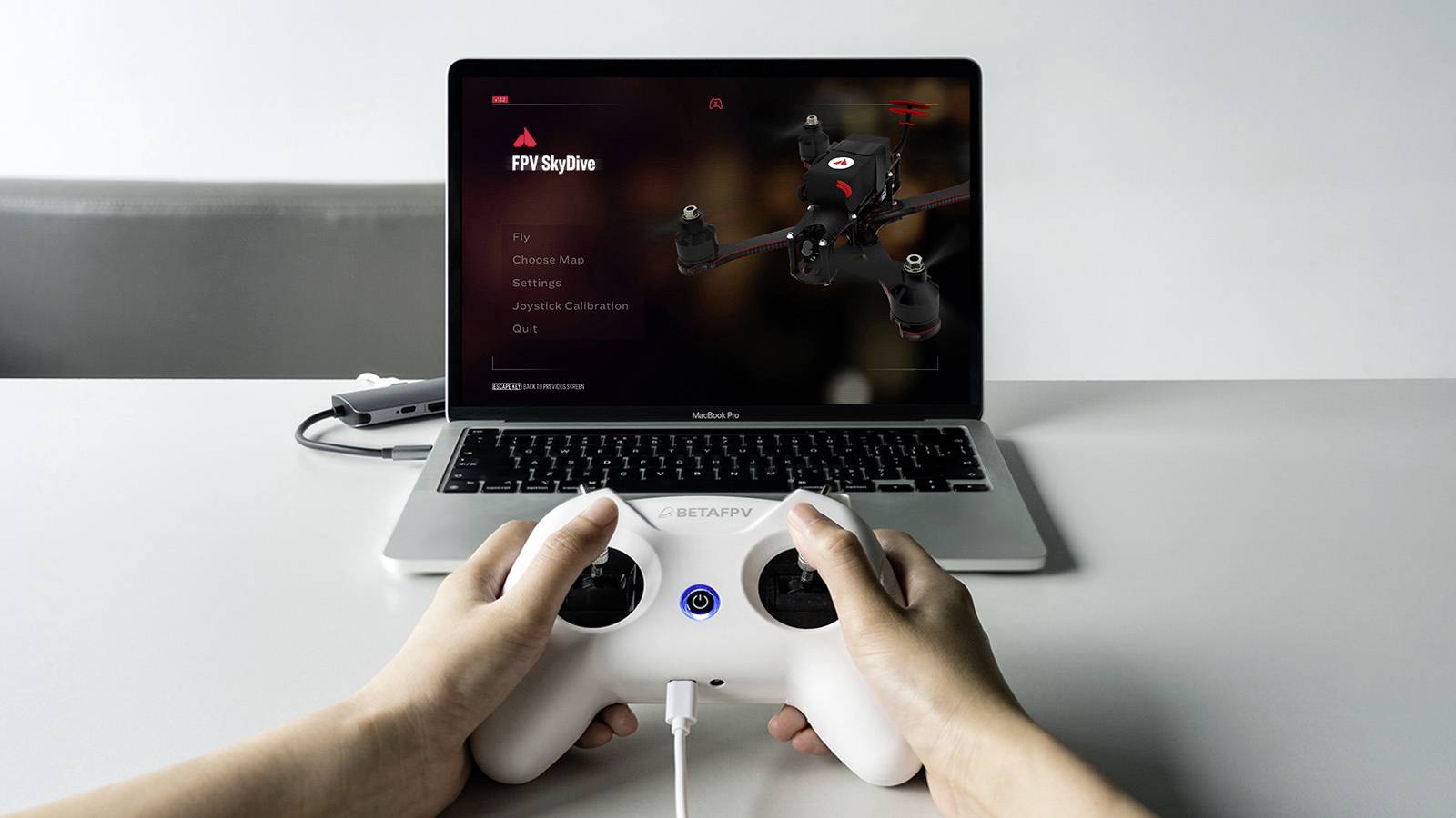 Eine Person steuert mit einem weißen Controller eine Drohne, auf einem Laptop-Bildschirm läuft eine Drohnensimulationssoftware.