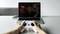 Eine Person steuert mit einem weißen Controller eine Drohne, auf einem Laptop-Bildschirm läuft eine Drohnensimulationssoftware.