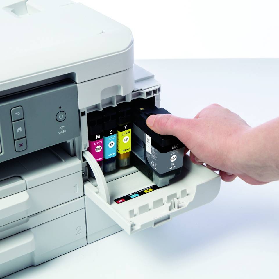 Eine Hand wechselt einen leeren Drucker-Tintentank aus einem Drucker. Der Drucker besitzt separate Tintentanks in Magenta, Cyan, Gelb und Schwarz.