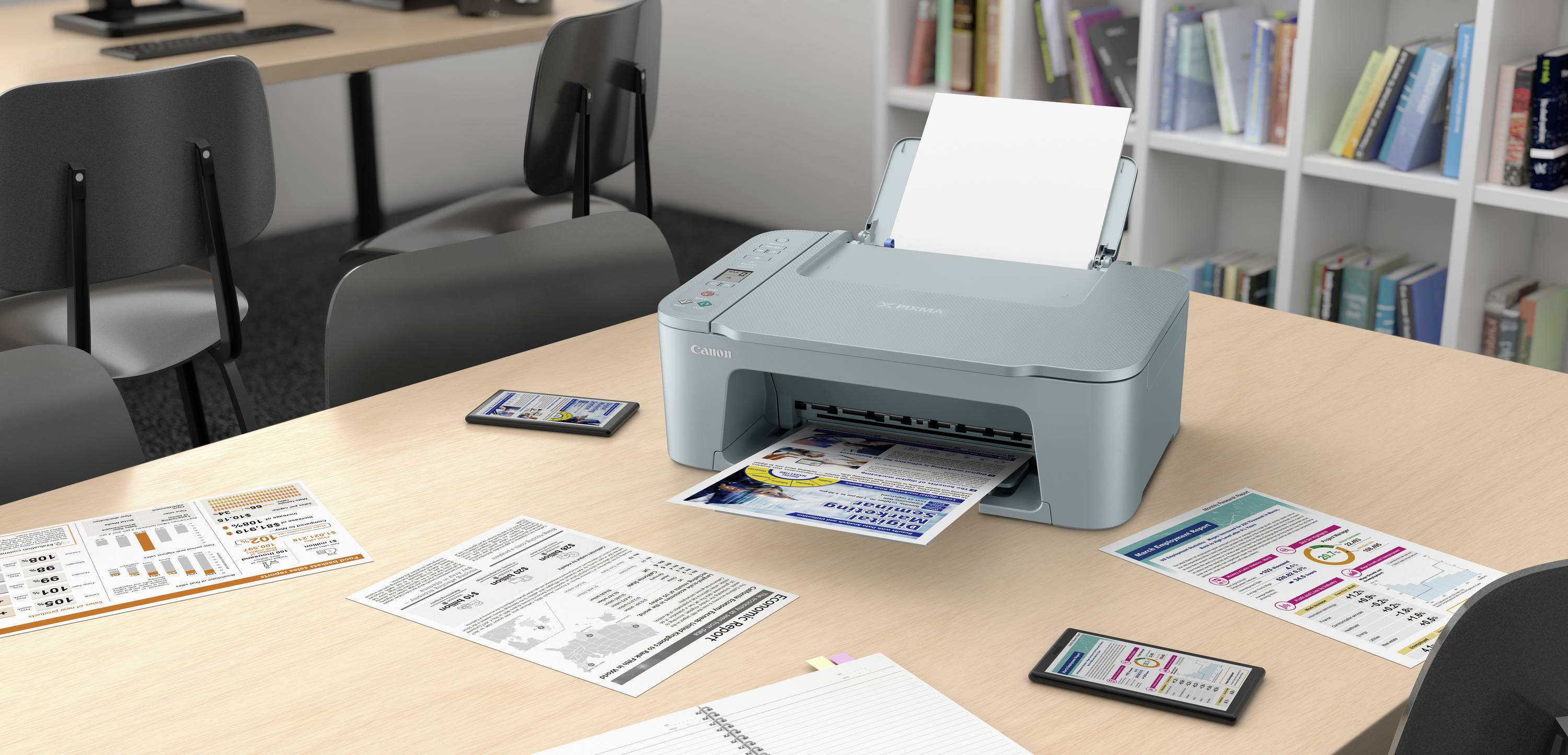 Ein Drucker auf einem Tisch druckt ein farbiges Dokument. Um den Drucker liegen verschiedene bunte Infoblätter und zwei Smartphones. Im Hintergrund stehen Bücherregale.