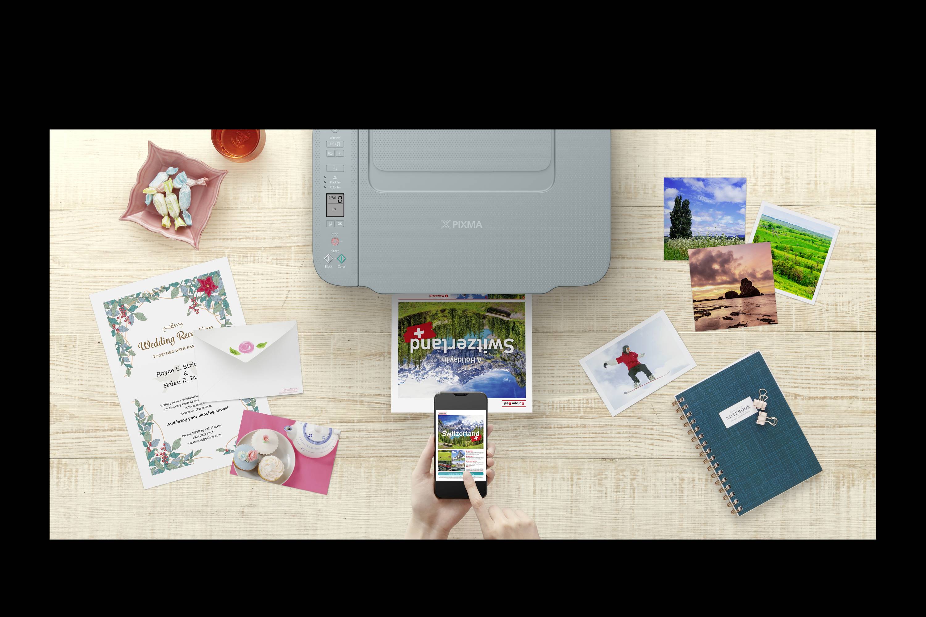 Drucker mit Smartphone-Fernsteuerung druckt ein Foto, umgeben von Hochzeitsprogramm, Fotos und einem Notizbuch auf einem Holztisch.