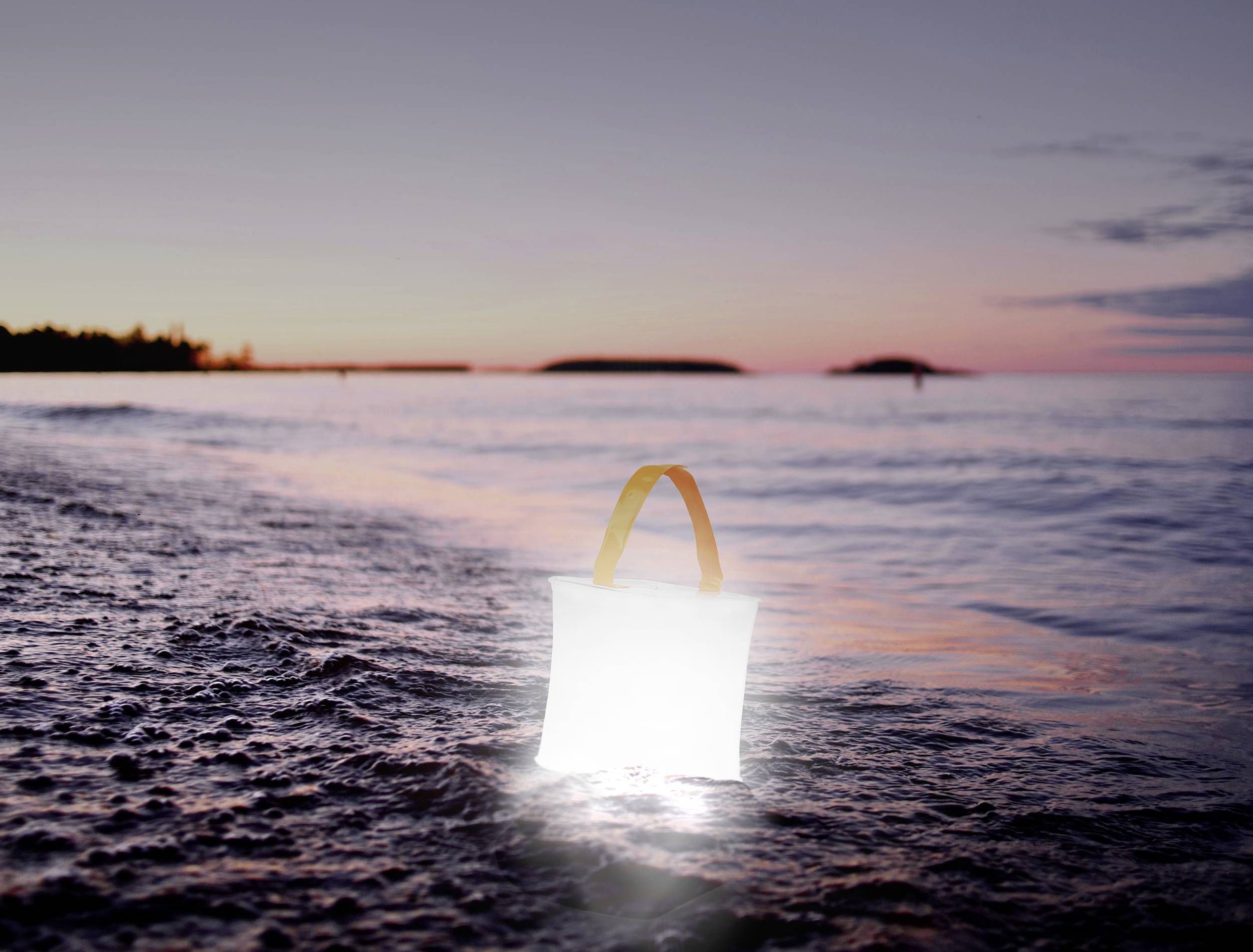 Eine leuchtende LED-Laterne steht am Ufer eines Strandes bei Sonnenuntergang, reflektiert im Wasser. Hintergrund: Meer und Inseln im Dämmerlicht.