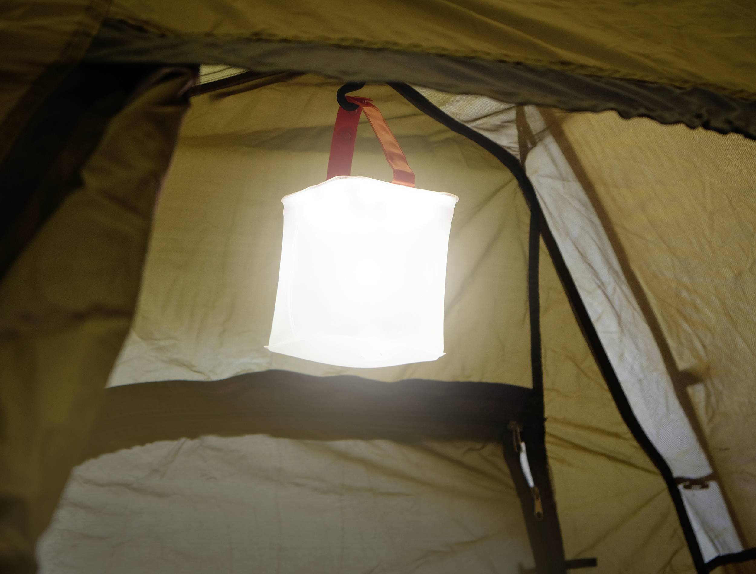 Eine leuchtende Laterne hängt im Inneren eines Zeltes und wirft warmes Licht auf die Zeltwände.
