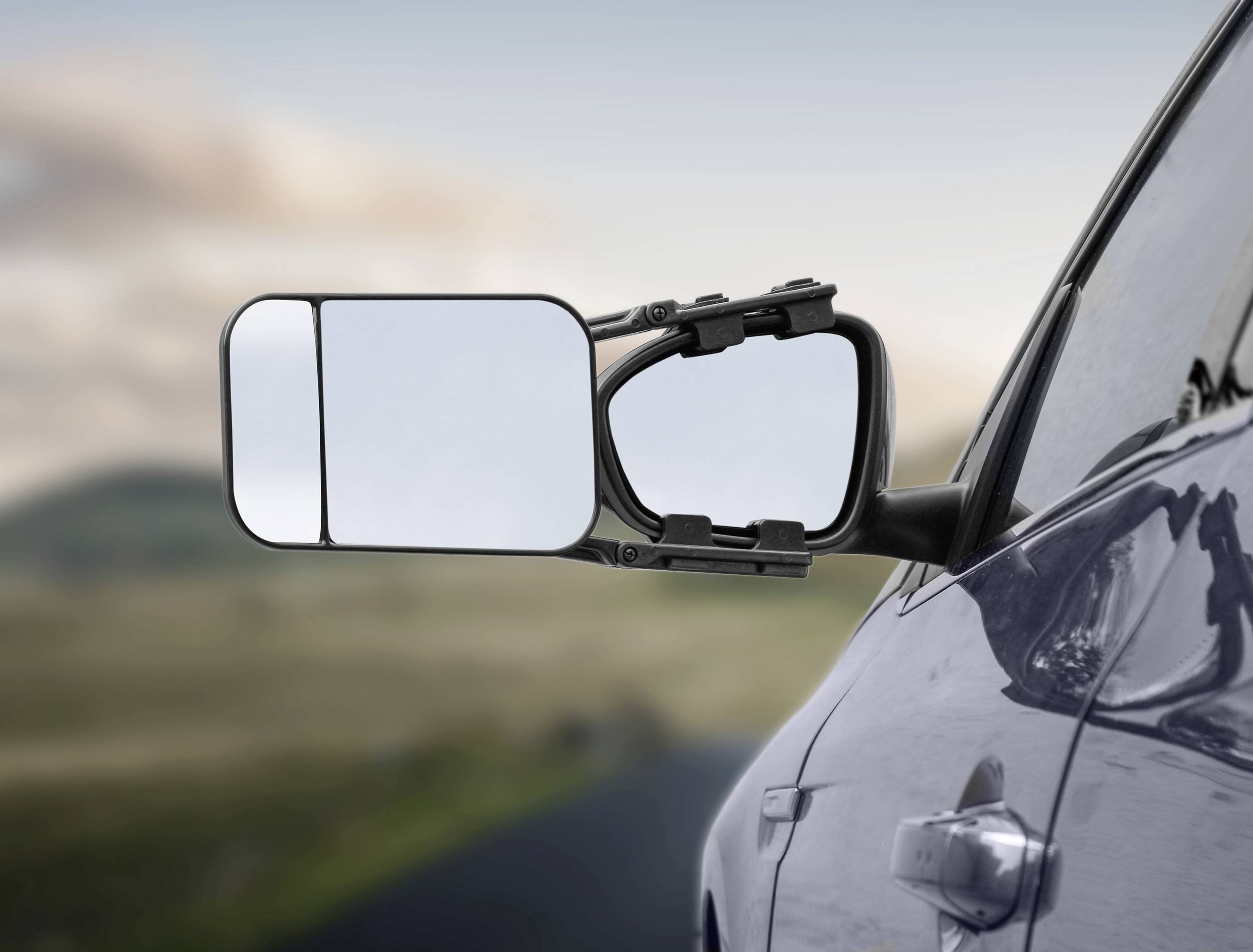 Auto mit erweitertem Außenspiegel für bessere Rücksicht beim Fahren. Landschaft im Hintergrund.