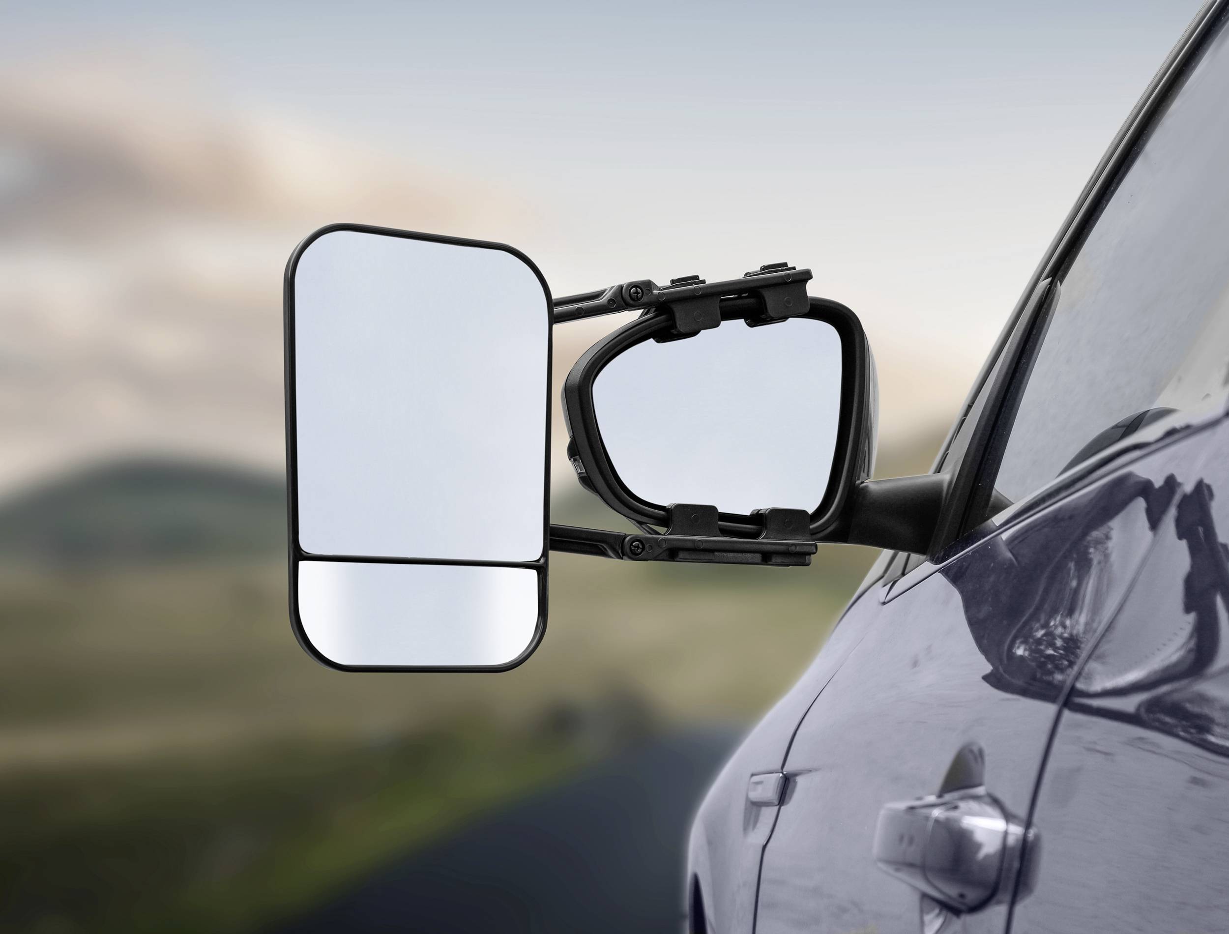 Ein Auto mit einem angebauten Wohnwagenspiegel steht am Straßenrand. Der Spiegel zeigt eine erweiterte Sicht nach hinten.