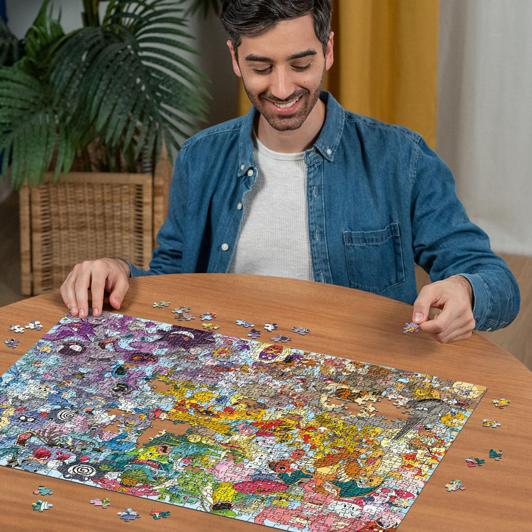Mann sitzt an einem Tisch und setzt ein buntes Puzzle zusammen. Im Hintergrund sind Pflanzen und helle Vorhänge zu sehen.