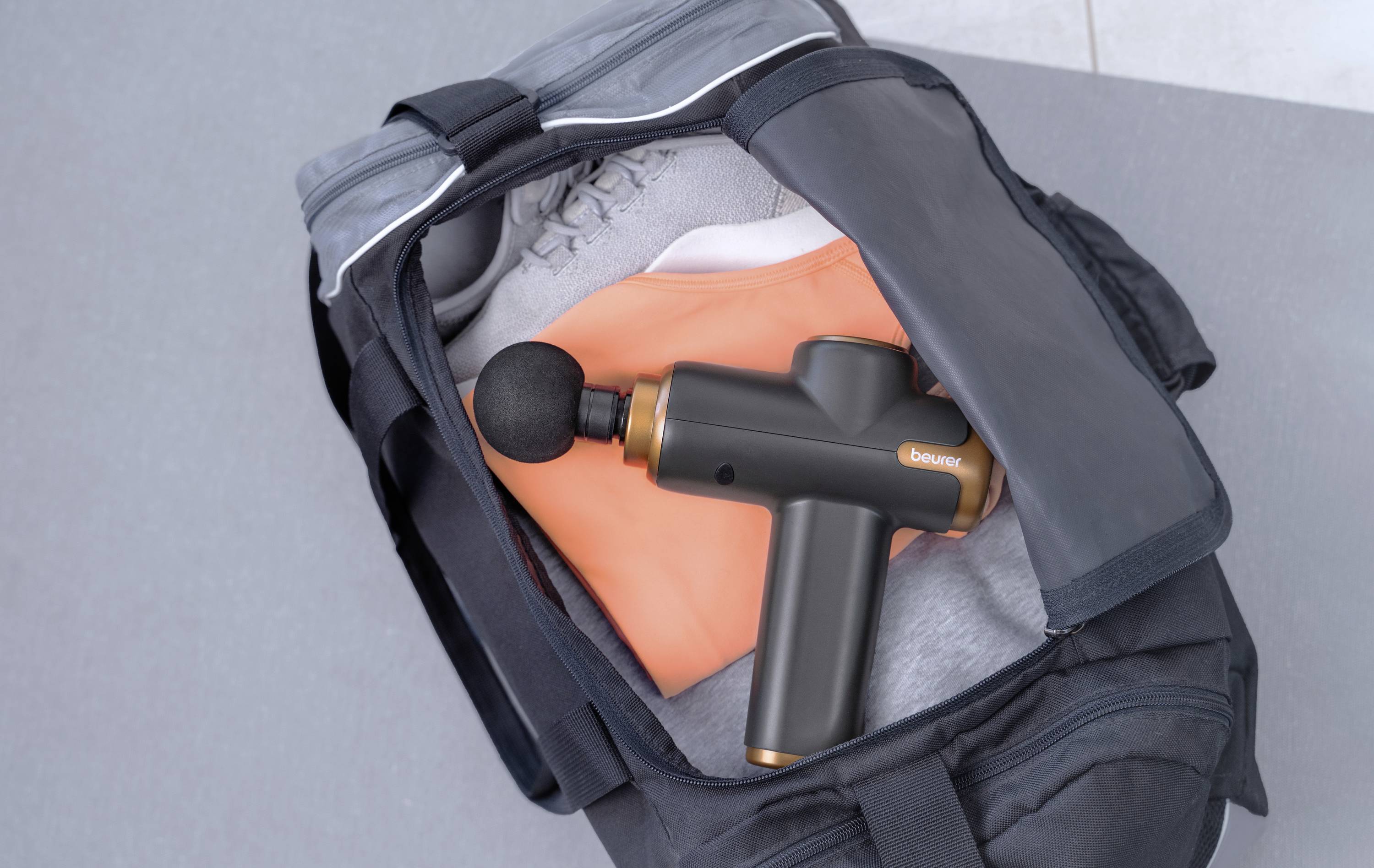 Eine schwarze Sporttasche mit einem Massagegerät, einem grauen Handtuch und einem orangefarbenen Kleidungsstück darin.