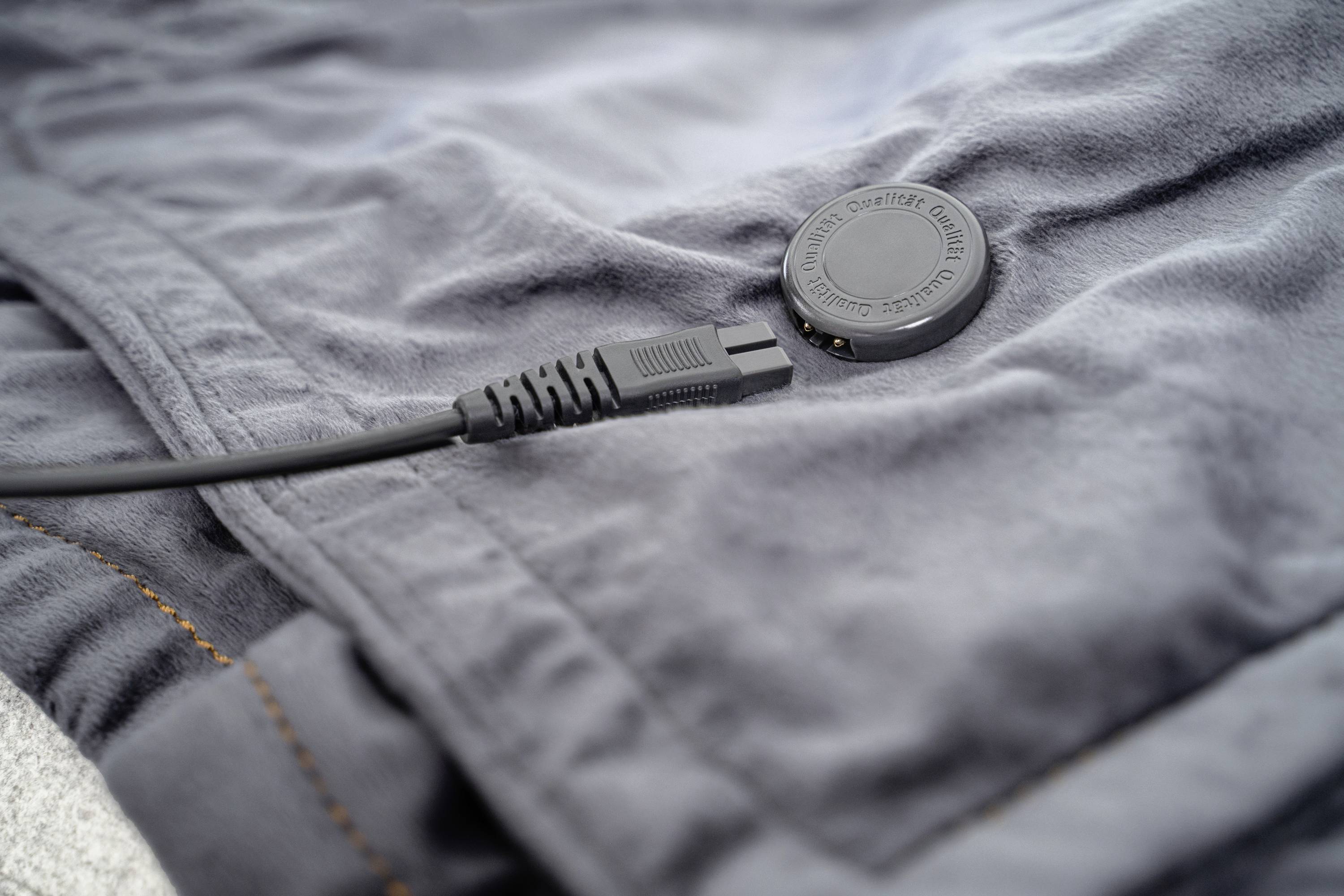 Ein schwarzes Ladekabel ist an ein rundes Ladegerät auf einem grauen Stoff angeschlossen. Es zeigt ein Beispiel für kabelloses Laden.