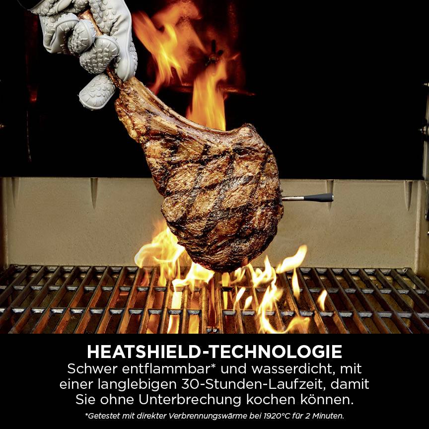 Eine Hand hält ein gegrilltes Steak über einem Grill mit Flammen. Text beschreibt Heatshield-Technologie, die wasserabweisend ist.