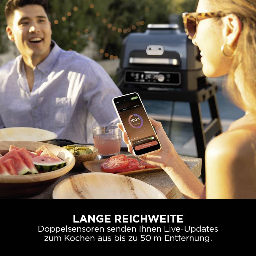 Eine Person zeigt auf ihrem Smartphone eine Grill-App, während im Hintergrund ein Grill zu sehen ist. Text: 'Lange Reichweite'.