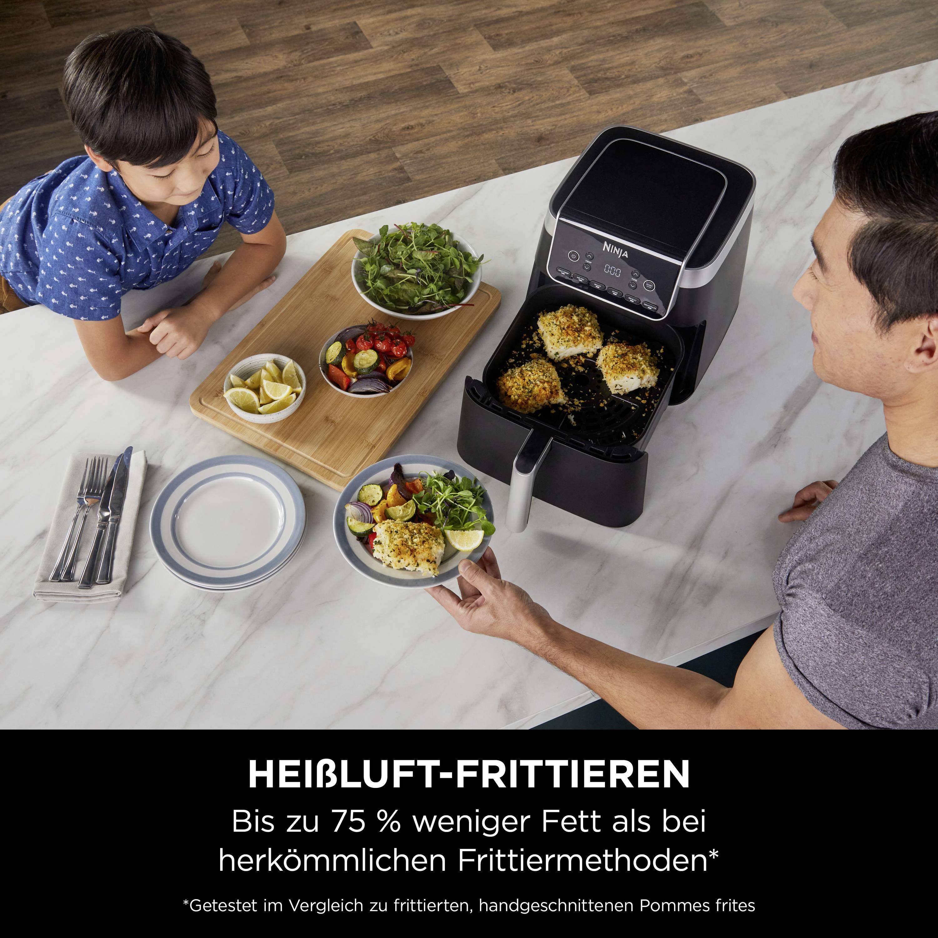Mann und Kind bereiten Essen mit einer Heißluftfritteuse vor. Text unten: 'HEISSLUFT-FRITTIEREN mit bis zu 75 % weniger Fett als bei herkömmlichen Methoden'.