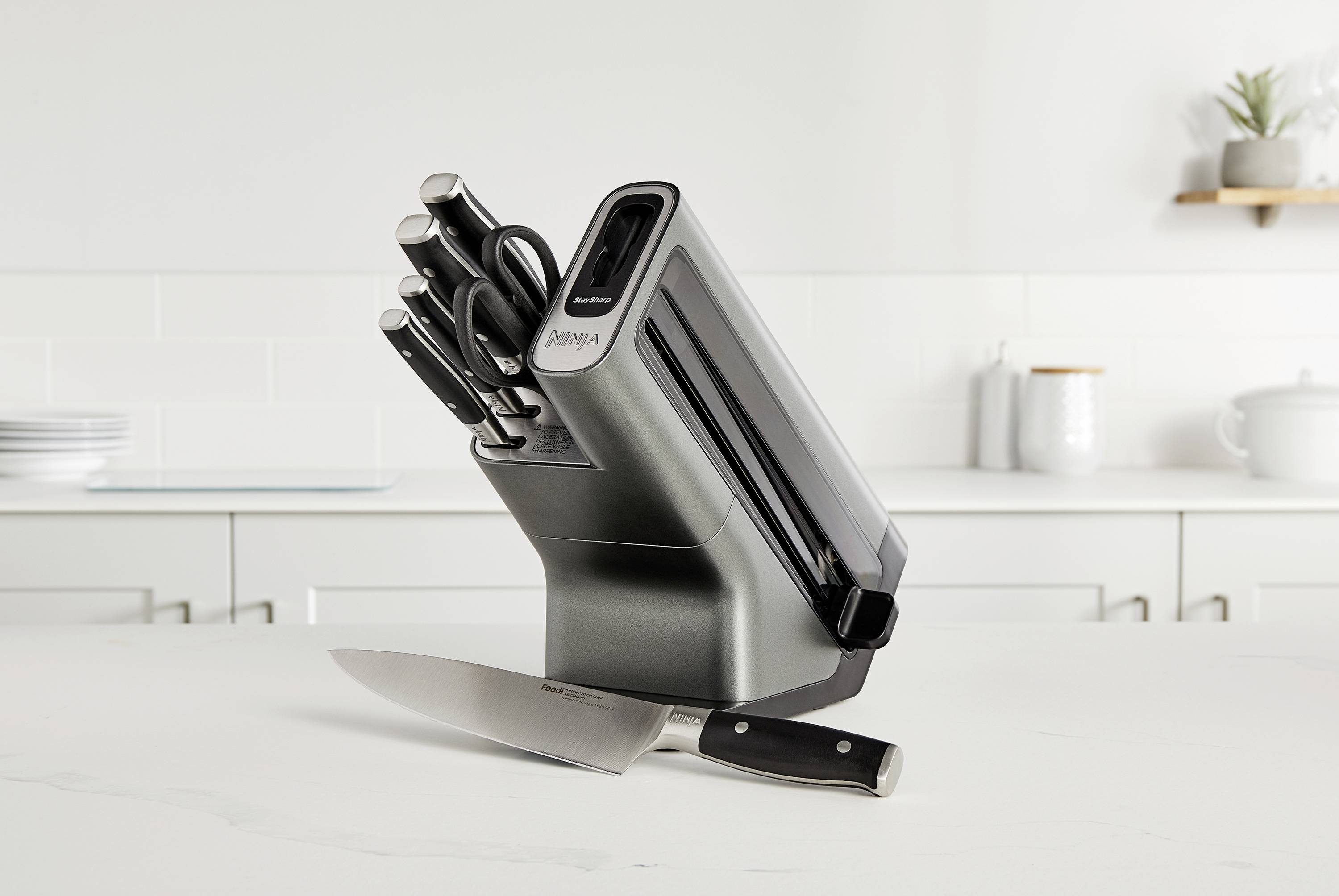 Ein Messerblock mit mehreren Messern steht auf einer weißen Küchenarbeitsplatte im modernen Design. Im Hintergrund sind Küchenutensilien.