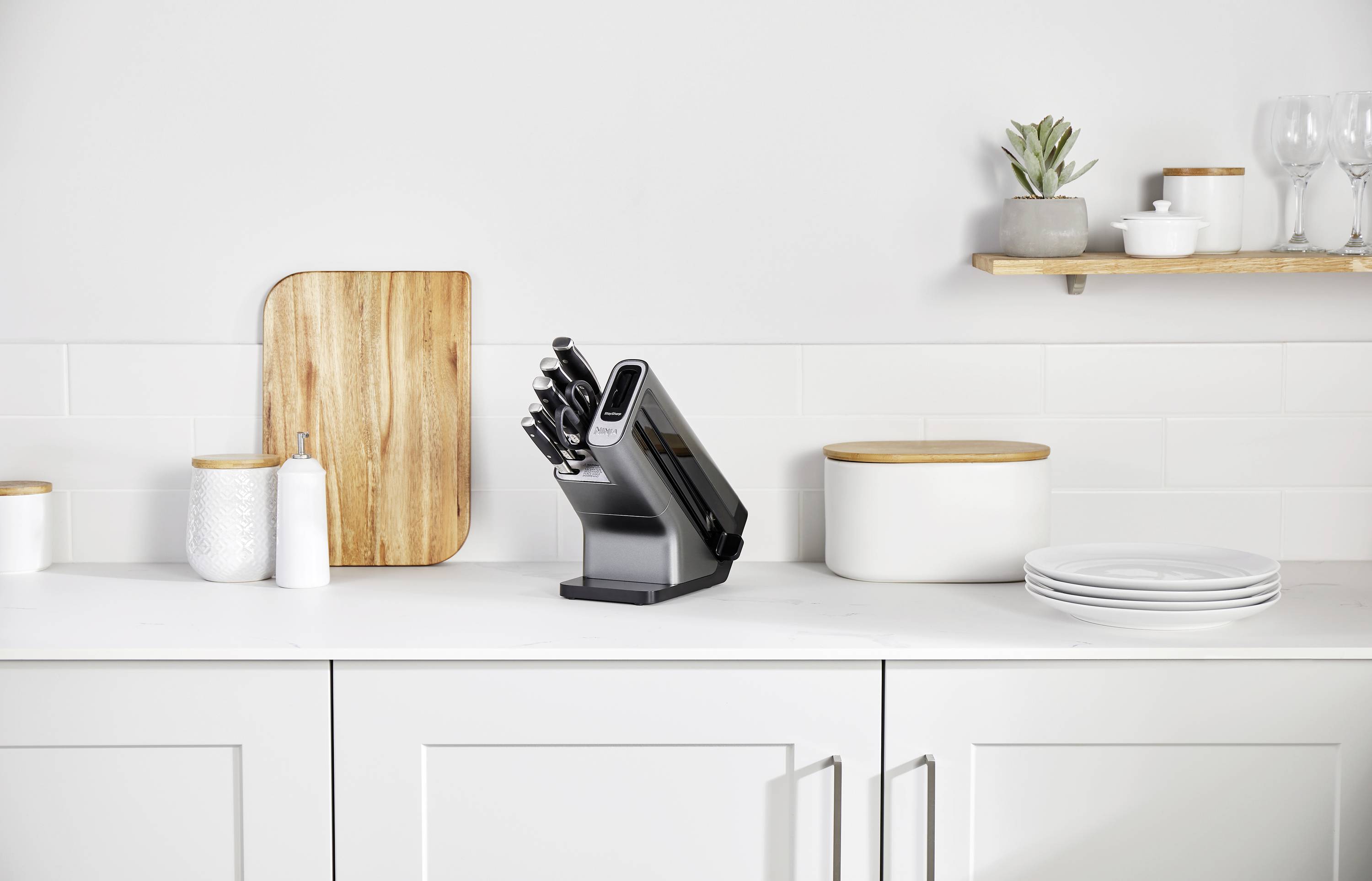Weiße Küche mit Messerblock, Schneidebrett und Geschirr auf Arbeitsplatte. Minimalistisches Design mit funktionalem Zubehör.