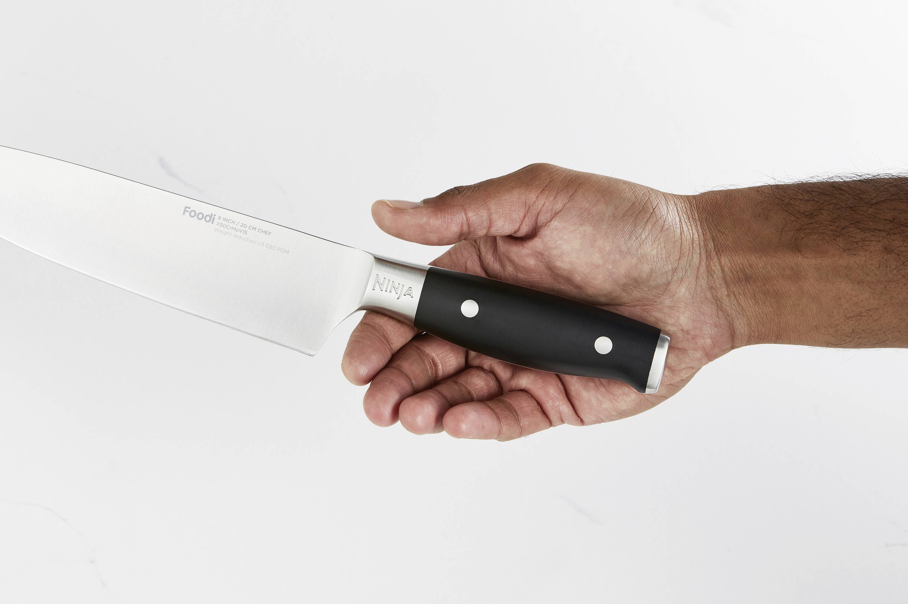Eine Hand hält ein Küchenmesser mit schwarzem Griff. Die Klinge zeigt nach links. Hintergrund ist neutral und einfarbig.
