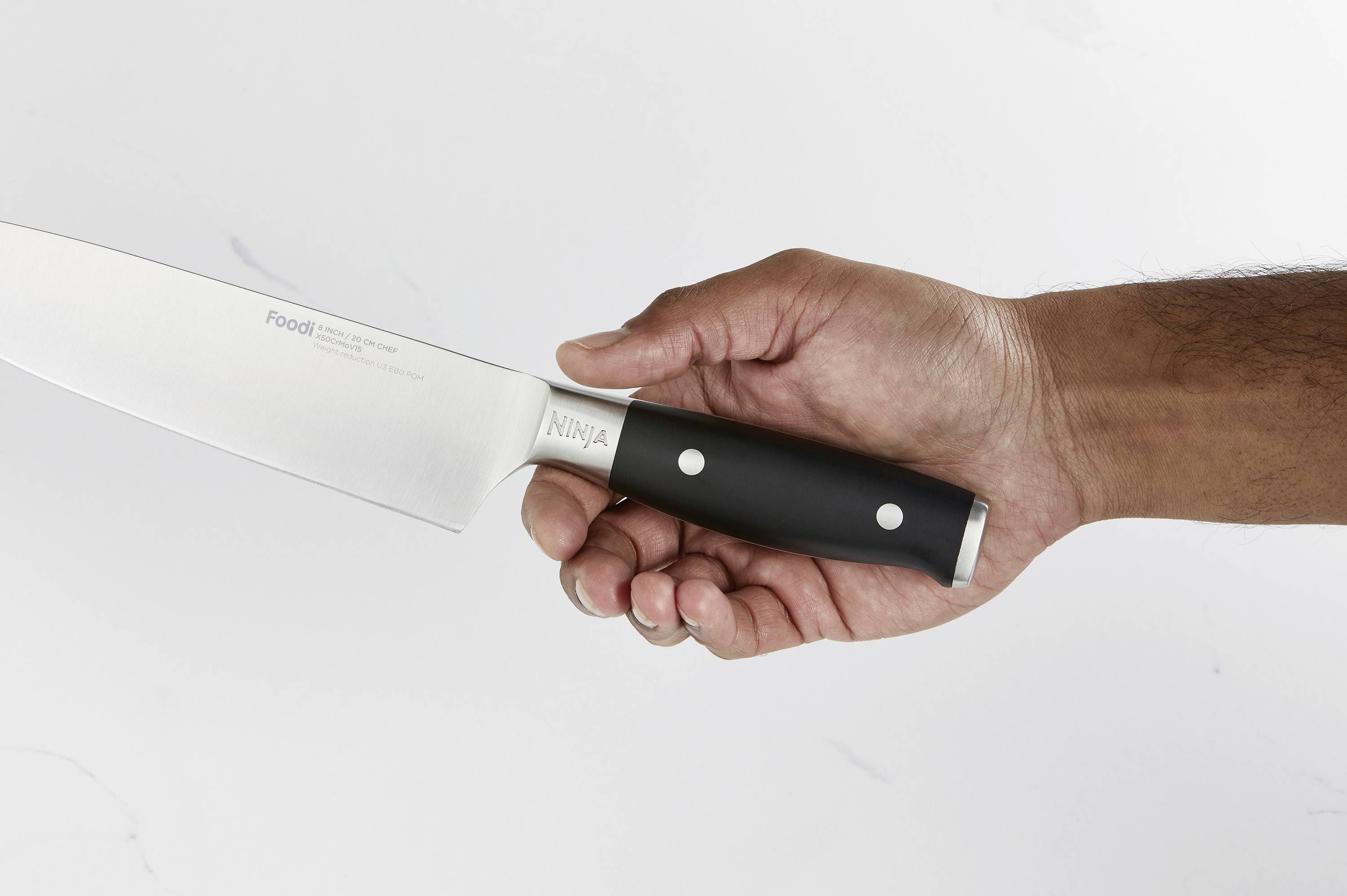 Eine Hand hält ein Küchenmesser mit schwarzem Griff. Der Hintergrund ist neutral und hell, was die Hand und das Messer betont.