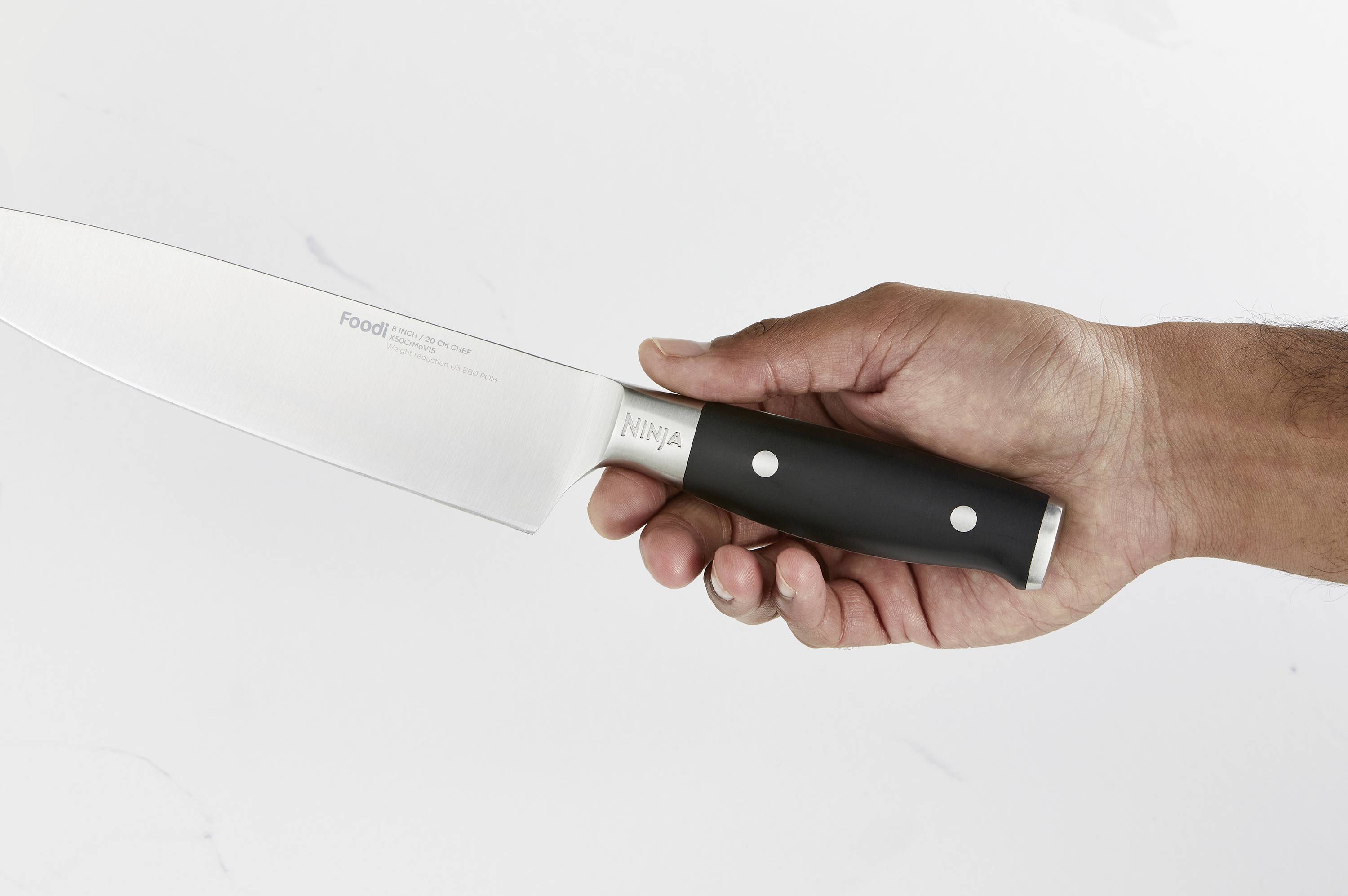 Eine Hand hält ein großes Küchenmesser mit schwarzem Griff, schwebend vor einem hellen Hintergrund.